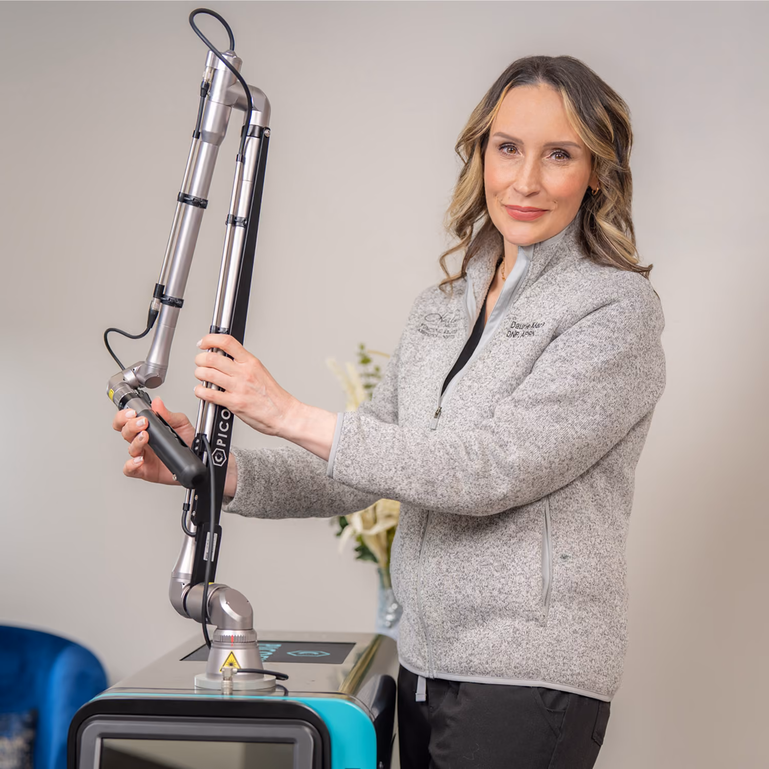 Woman in gray jacket adjusting a PICO laser machine arm in a clinical setting.