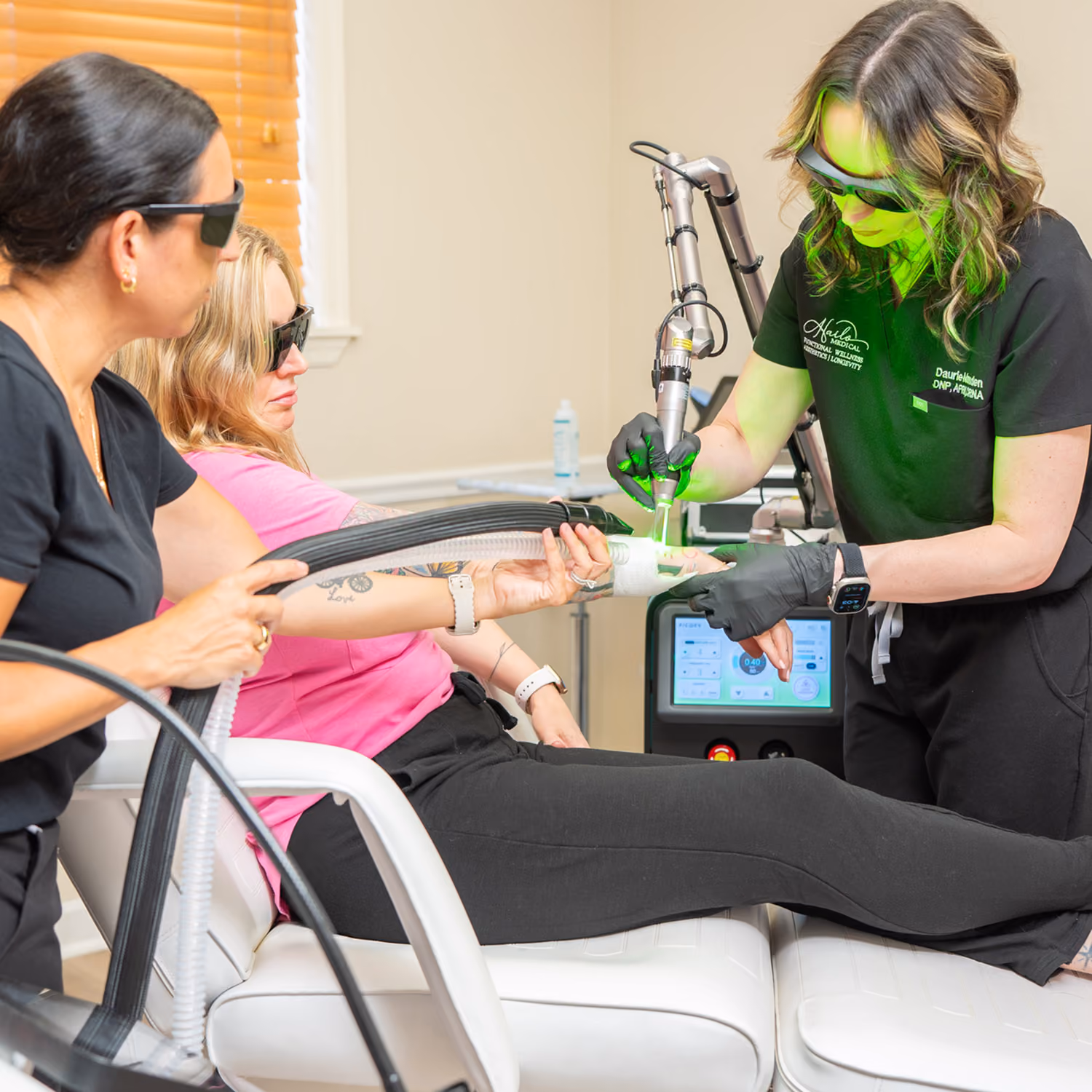 Woman in pink gets laser treatment on her forearm from a specialist wearing black gloves and glasses.