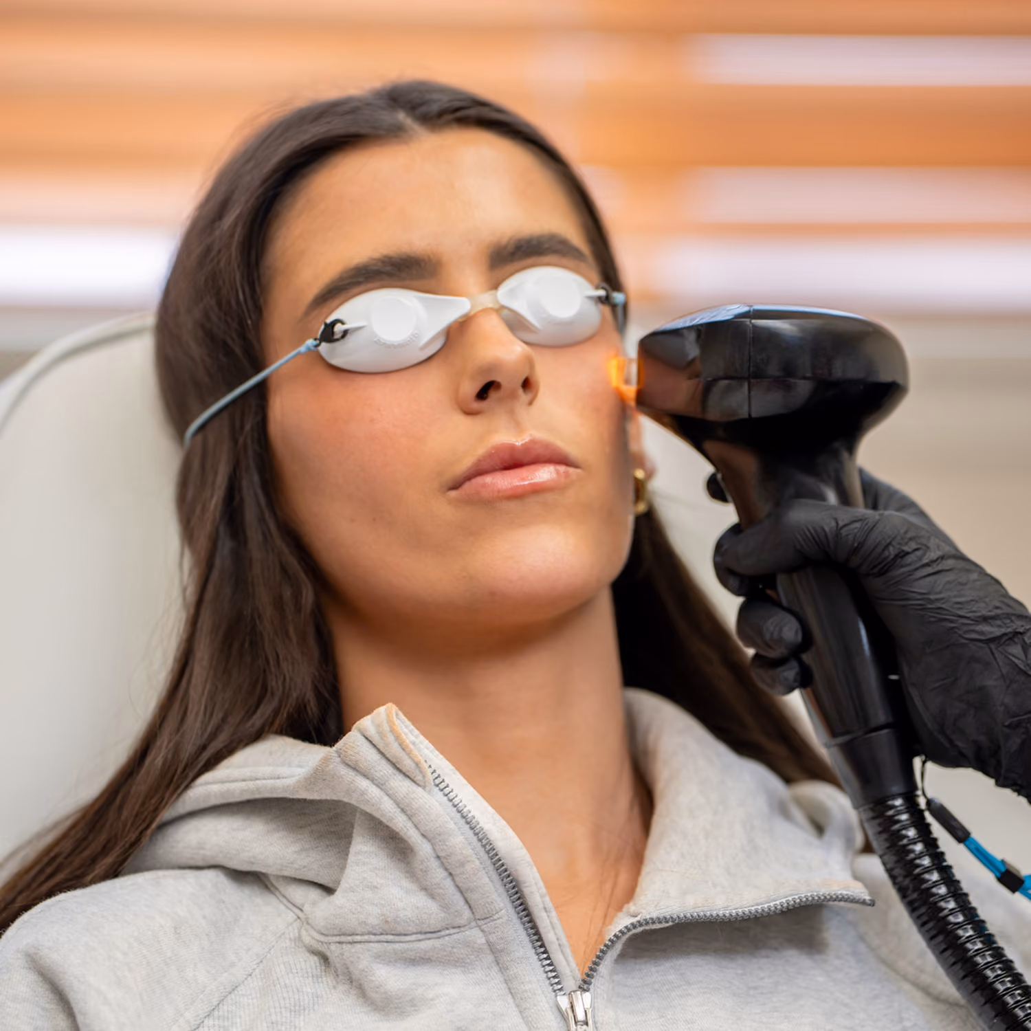 Woman wearing protective goggles receiving facial laser treatment from a gloved professional.