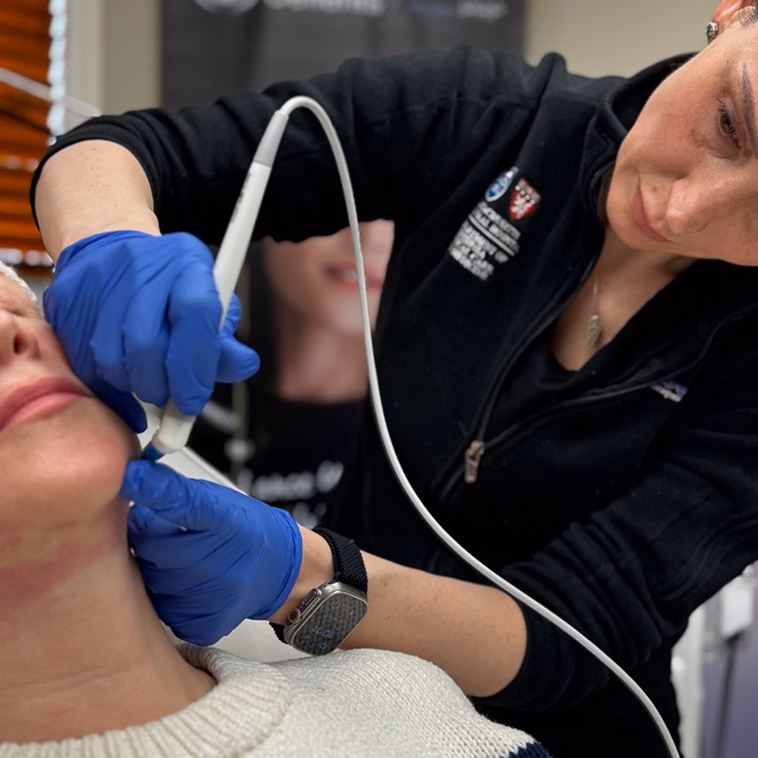 Professional wearing blue gloves performs skin treatment on patient's chin with a handheld device.
