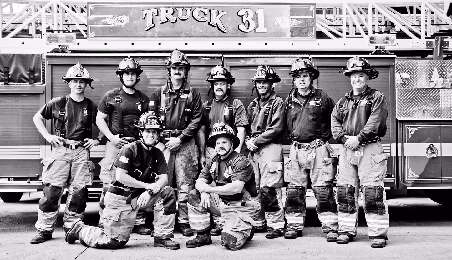 Group of nine firefighters in uniform posing in front of fire truck labeled Truck 31.