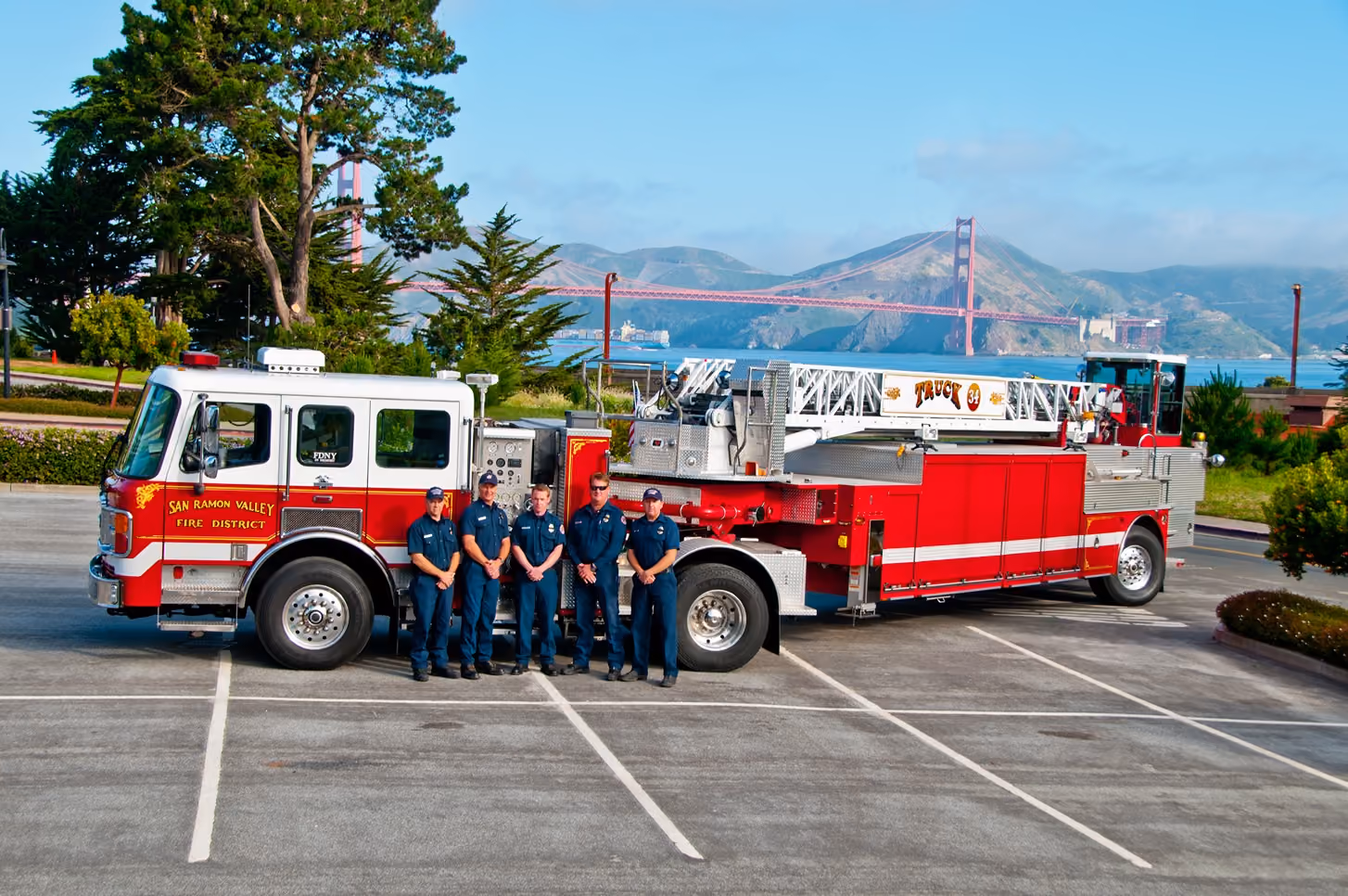 Five firefighters standing in front of a red San Ramon Valley Fire District truck with Golden Gate Bridge in background.