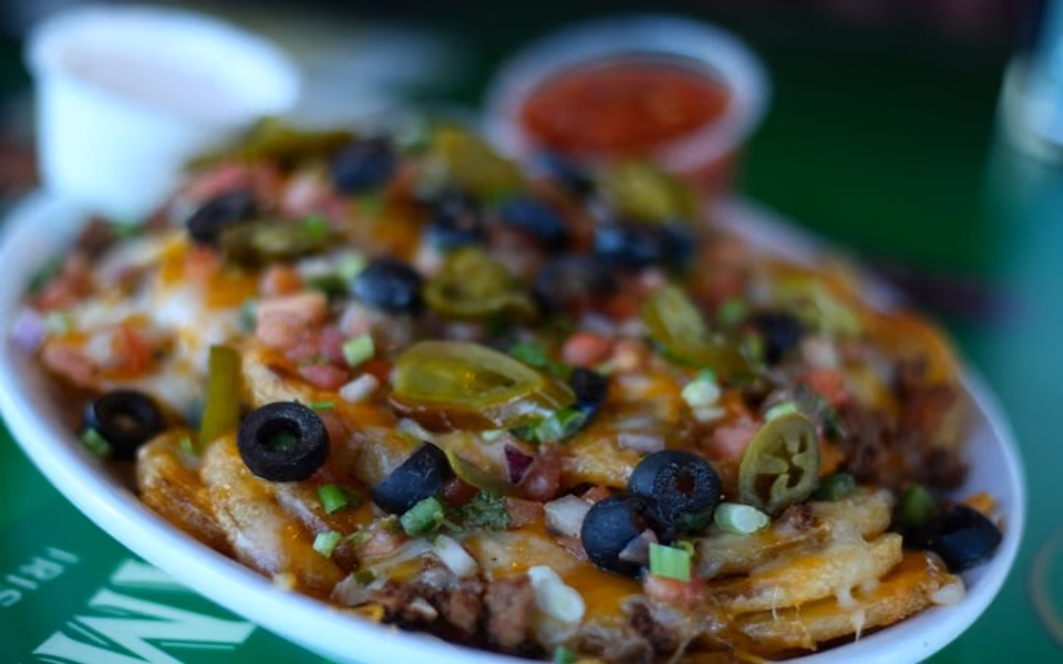 Plate of loaded nachos topped with olives, jalapeños, cheese, tomatoes, and green onions with a side of salsa.