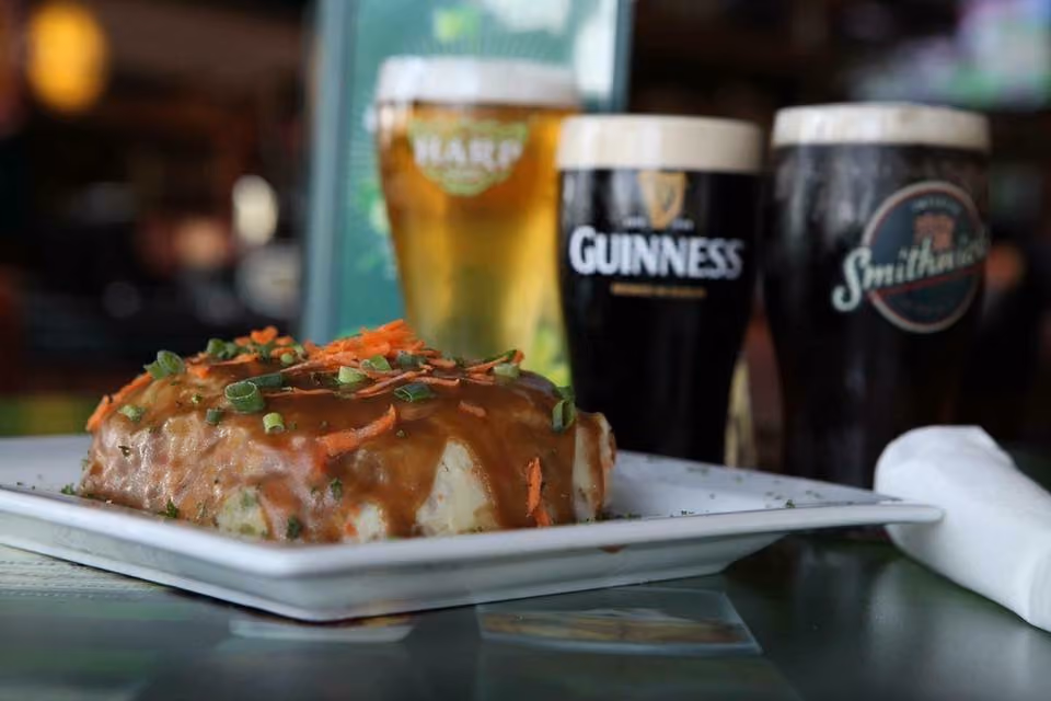 Mashed potatoes with brown gravy and chopped green onions served on a white plate with three pint glasses of beer.