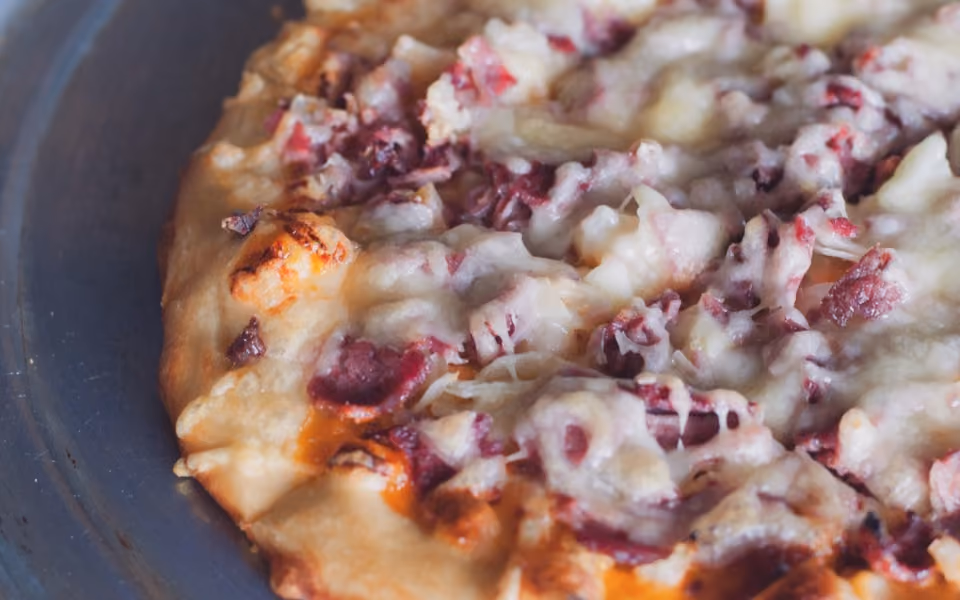 Close-up of a pizza with melted cheese and diced meat on a metal tray.