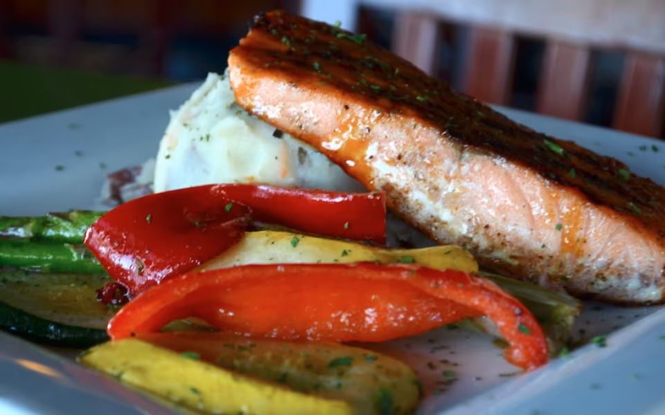 Grilled salmon fillet served with mashed potatoes and colorful sautéed vegetables on a plate.