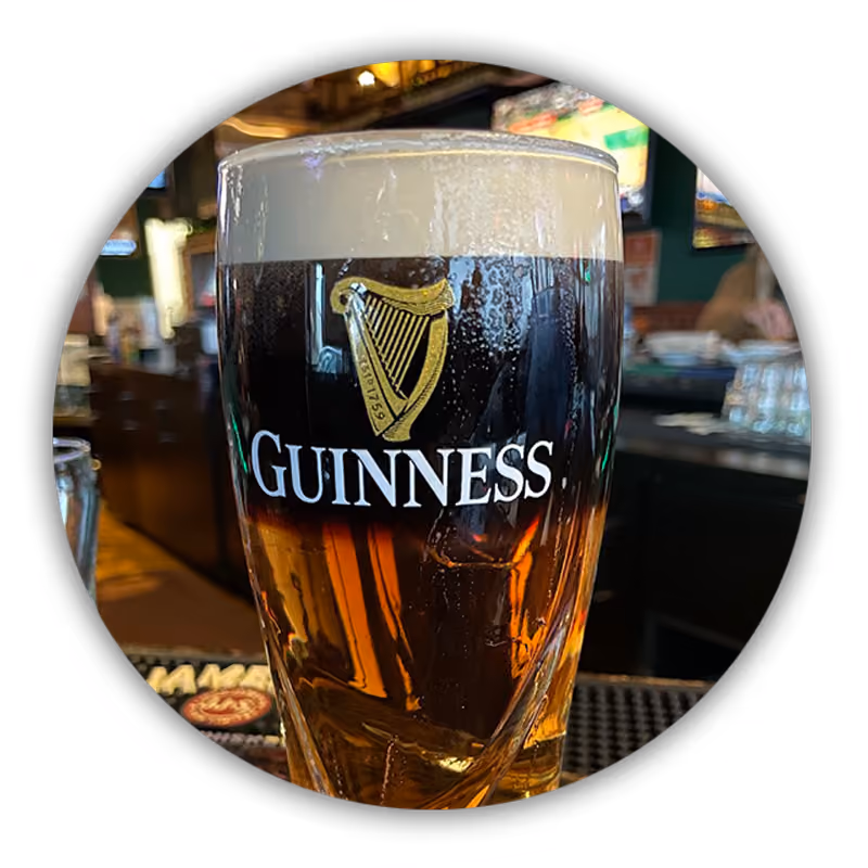 A pint of Guinness beer with a creamy head on a bar counter in a pub setting.
