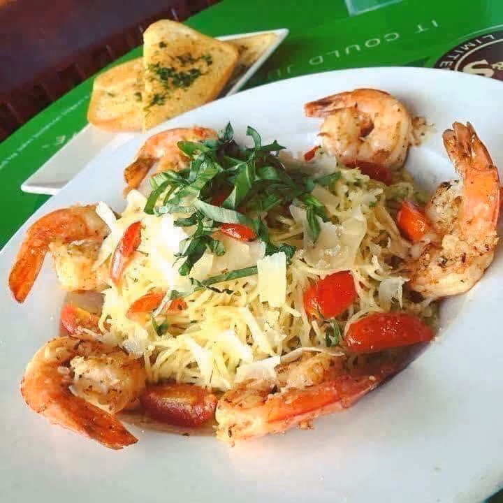 Plate of shrimp pasta with cherry tomatoes, fresh basil, and grated cheese, served with garlic bread on the side.