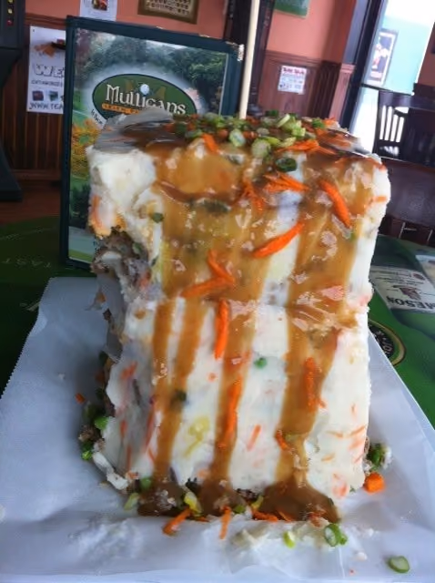 A tall layered mashed potato dish topped with gravy, chopped green onions, and shredded carrots on a white plate.