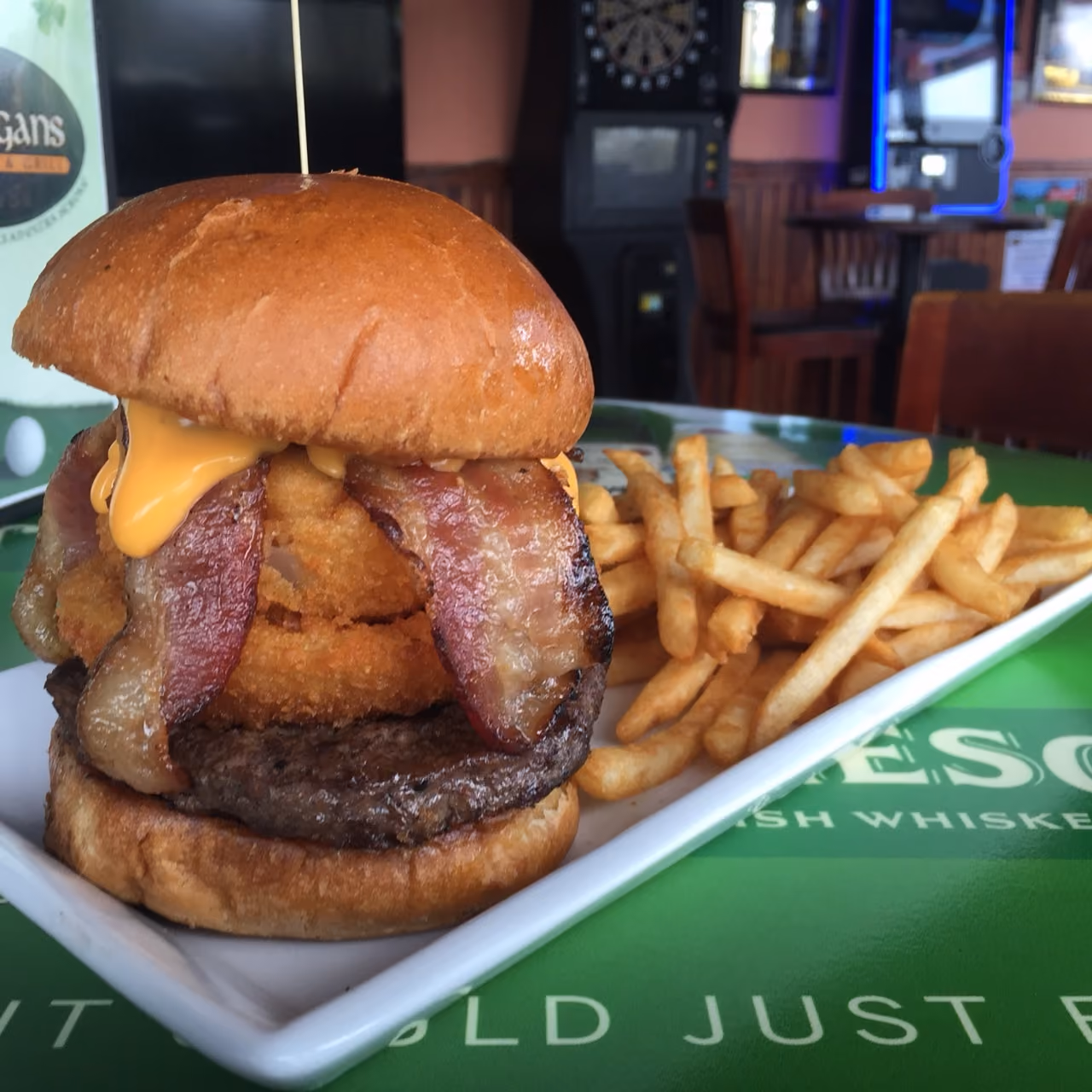 Burger with bacon, cheese, and onion rings served with French fries on a white plate.