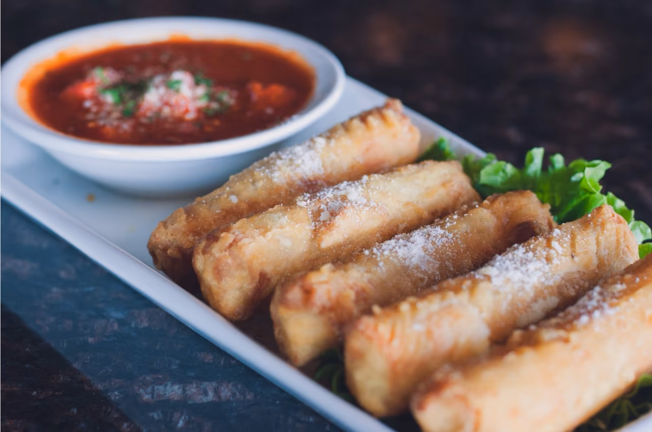Plate with fried mozzarella sticks sprinkled with cheese and a side of marinara sauce in a bowl.