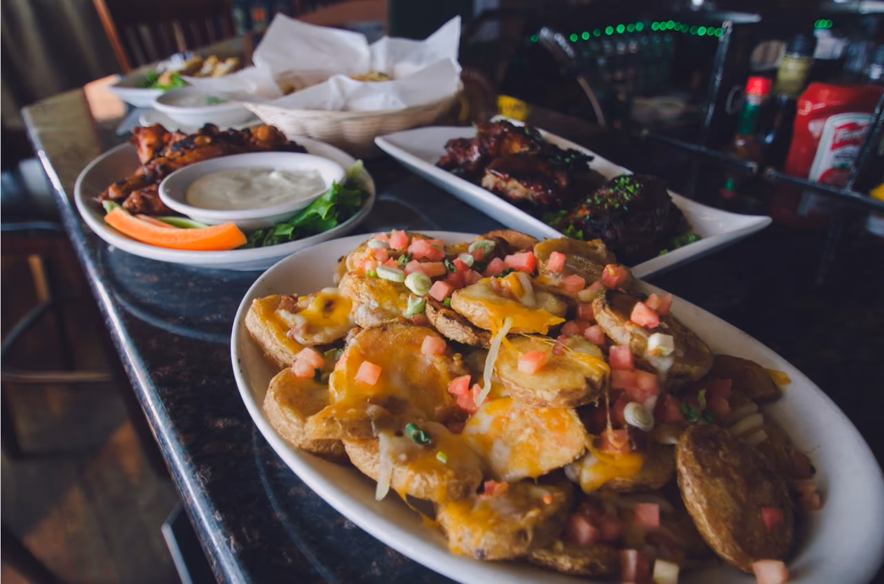 Plates of seasoned potato skins with cheese and diced tomatoes, and chicken wings with dipping sauce.