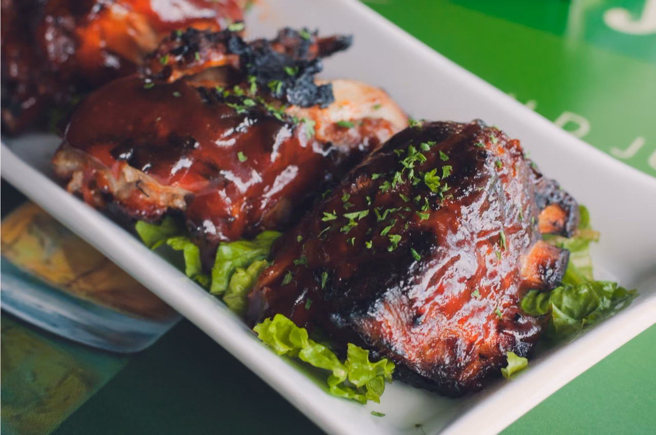 Barbecue ribs glazed with sauce, garnished with chopped herbs, on lettuce in a white dish.