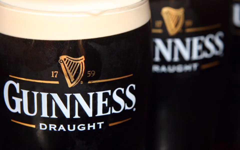 Close-up of a Guinness Draught beer glass with a foamy head and a blurred glass behind it.