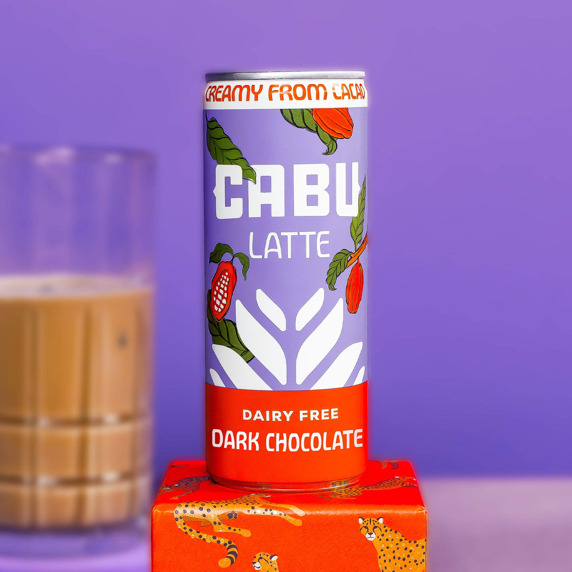 A can of CABU LATTE creamy from cacao, dairy free dark chocolate, standing on an orange box with cheetah prints against a purple background.