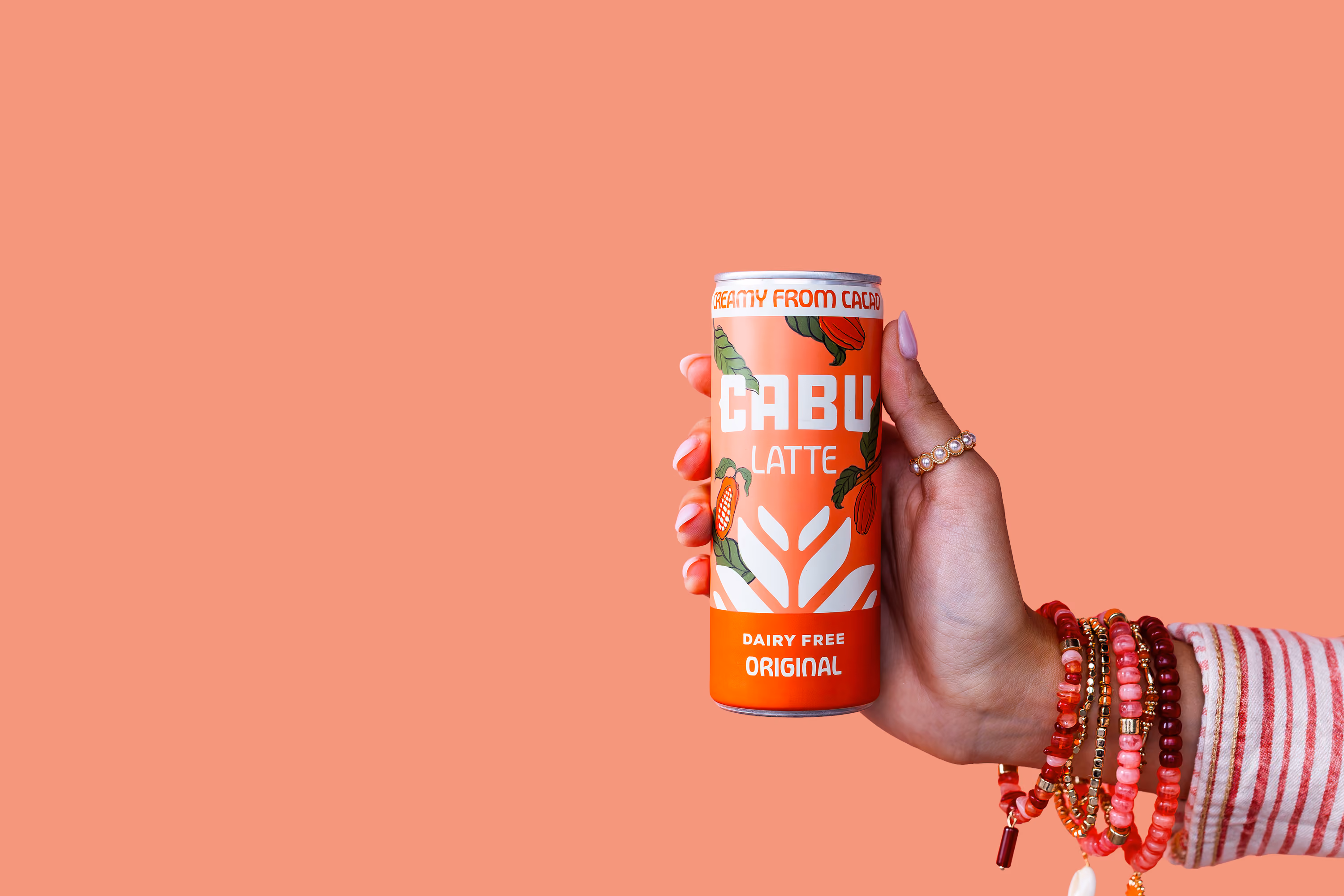 Hand with colorful bracelets holding an orange can of Cabu Latte dairy-free original drink.