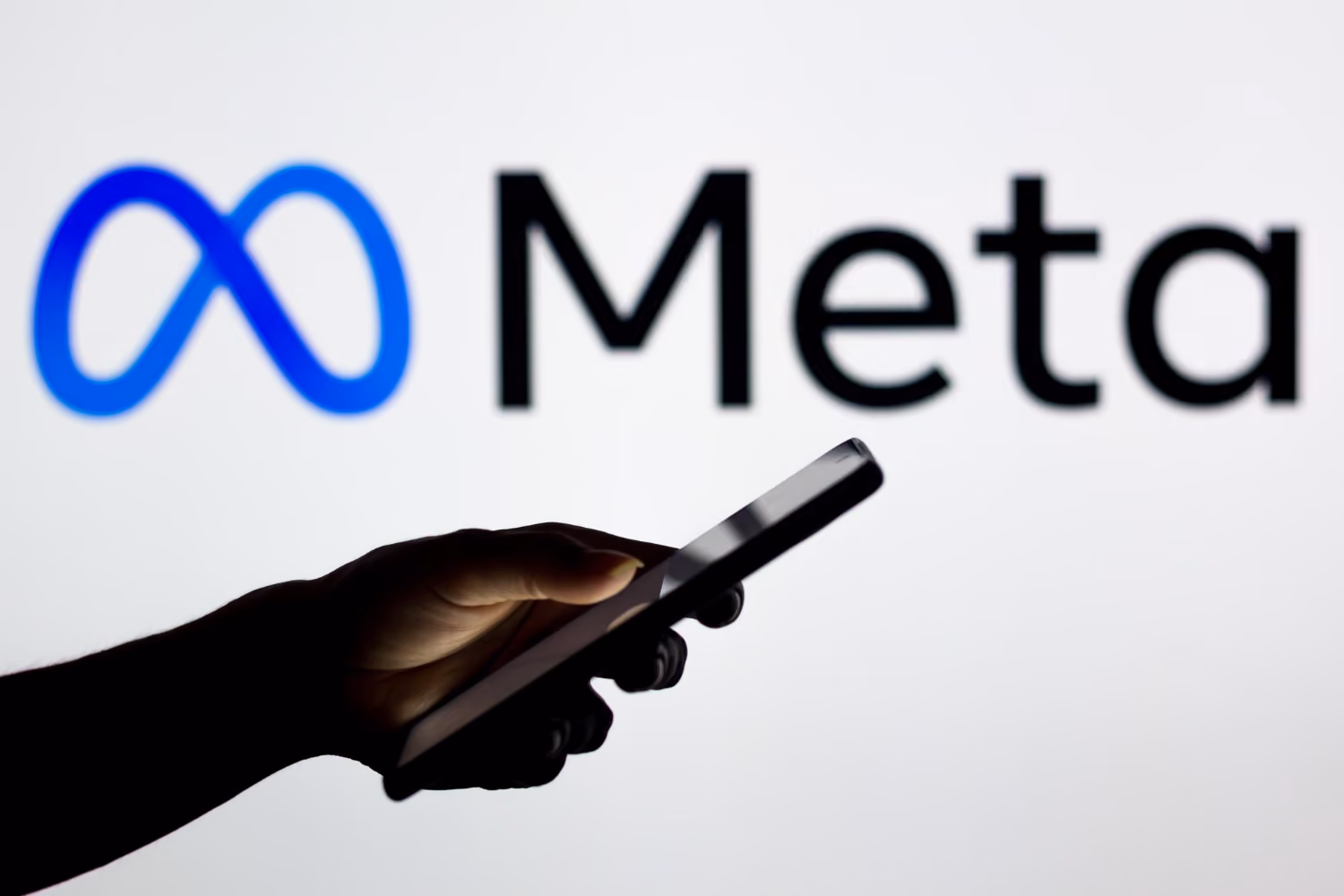 Hand mit Smartphone vor dem Meta-Logo