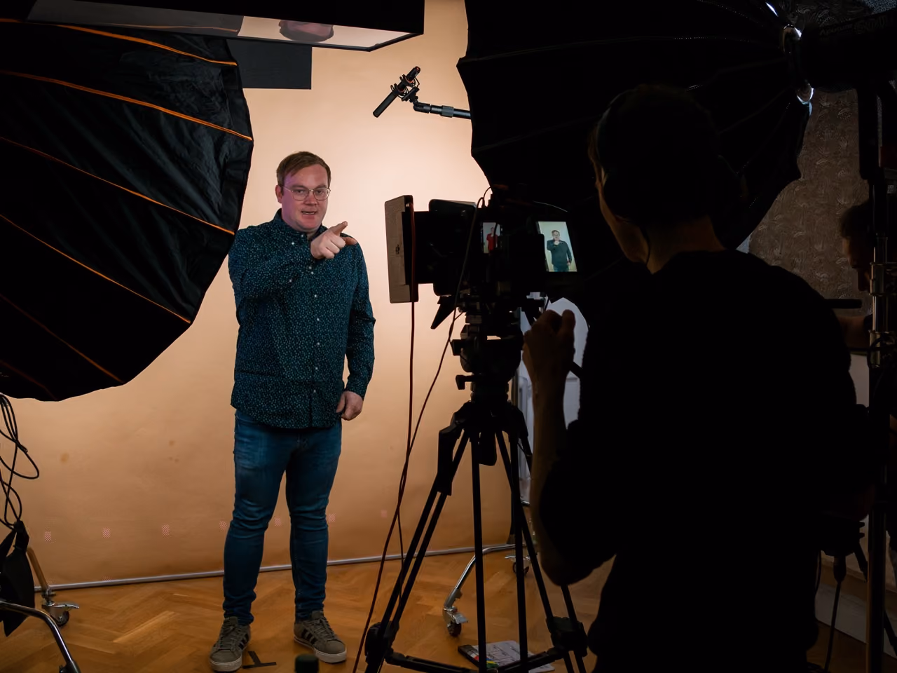 Man pointing and speaking in a studio setup with camera, lights, and crew filming him.