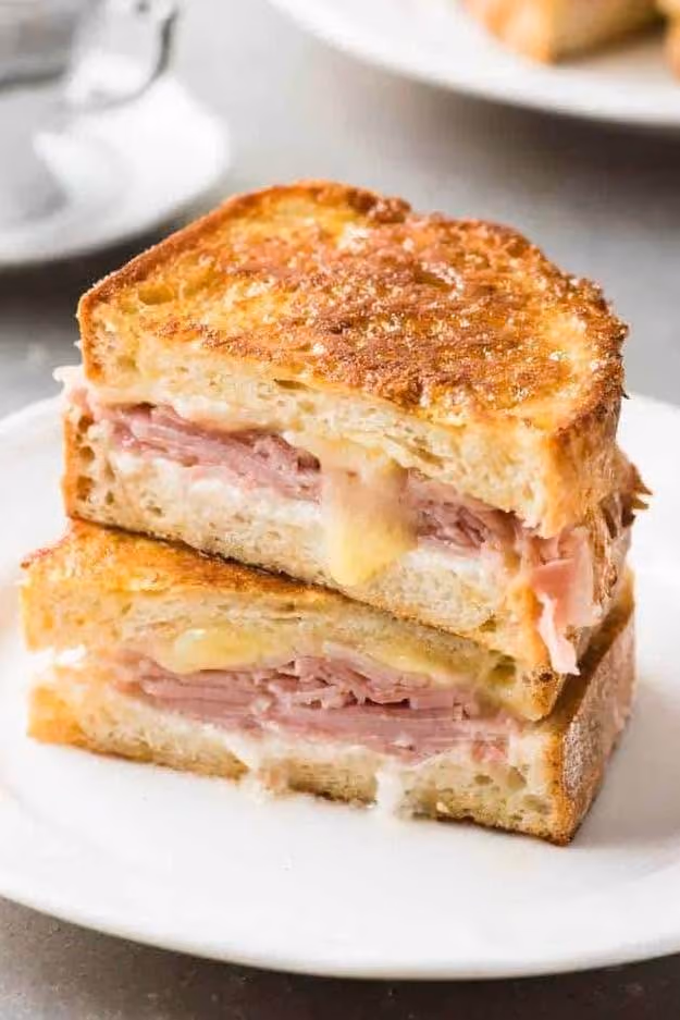 Grilled ham and melted cheese sandwich cut in half on a white plate.