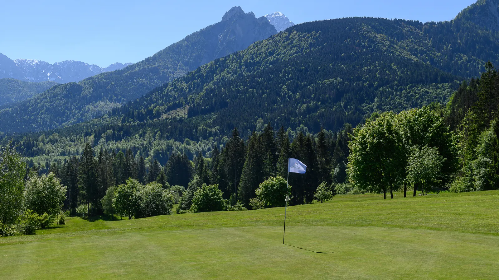 Golfgrün mit Fahne und Alpenpanorama am Golfclub Senza Confini