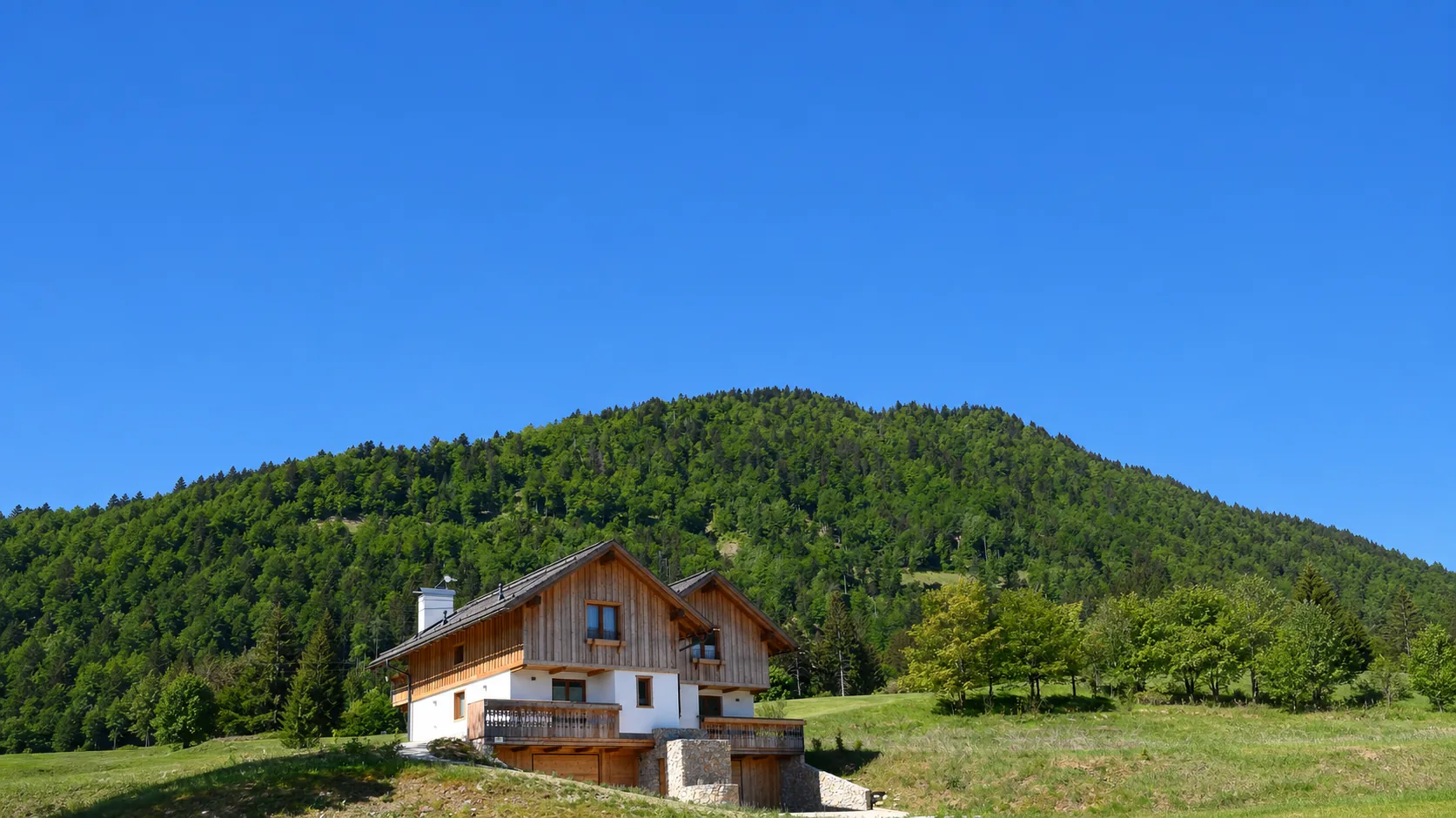 Golf-Chalet in Tarvisio vor bewaldeter Bergkulisse und weitem blauem Himmel
