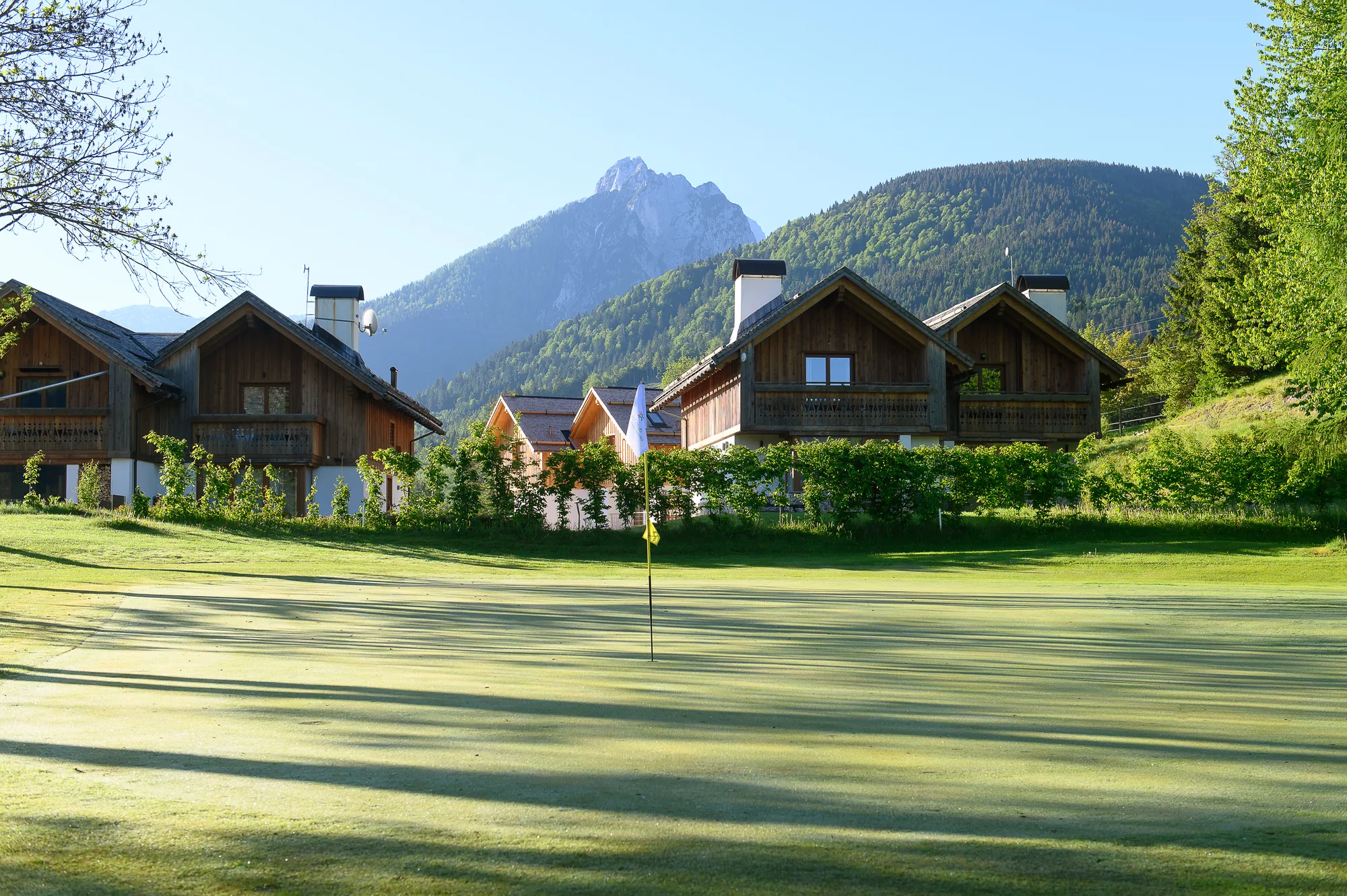 Golfgrün mit Fahne vor alpinen Chalets und Bergen