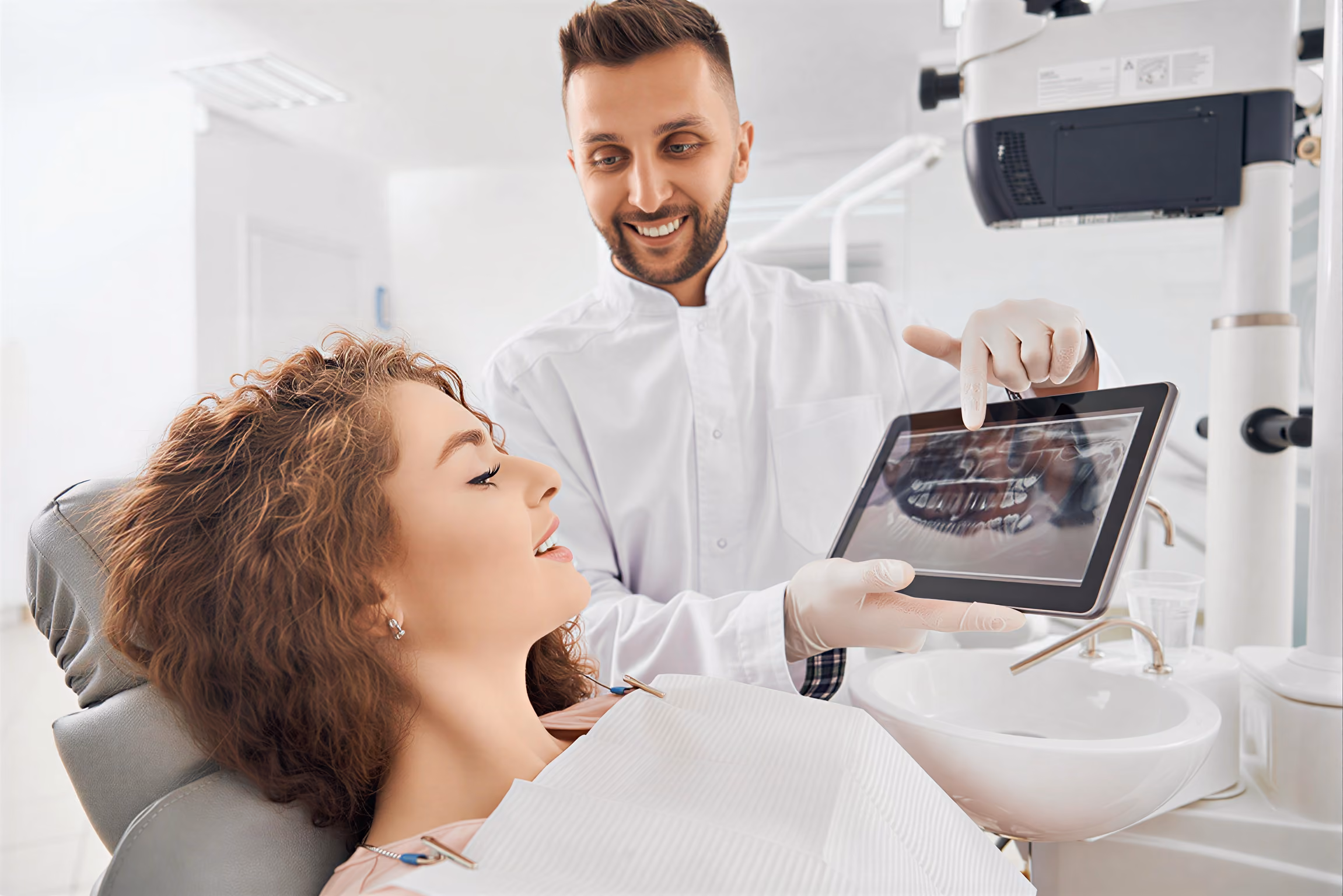 Dentist showing a dental x-ray on a tablet to a female patient reclining in the dental chair.
