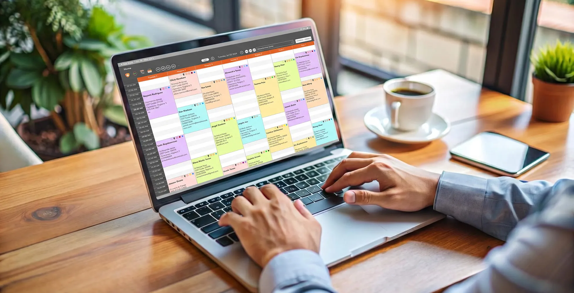 Person using laptop showing a colorful digital calendar or schedule on screen by a coffee cup and phone.