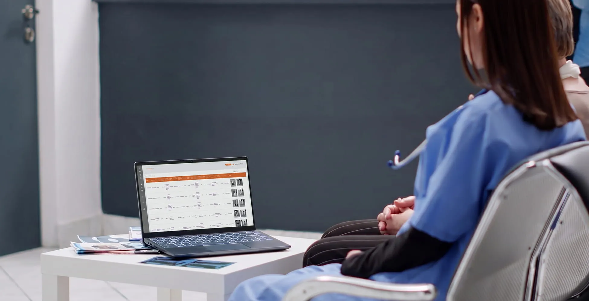 Two medical professionals sitting and looking at a laptop displaying patient scan records.