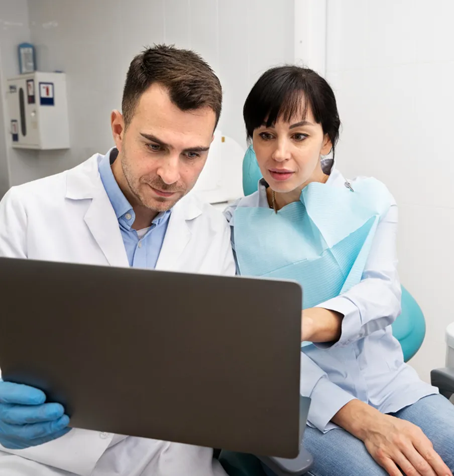 Male dentist and female patient reviewing information on a laptop in a dental clinic.