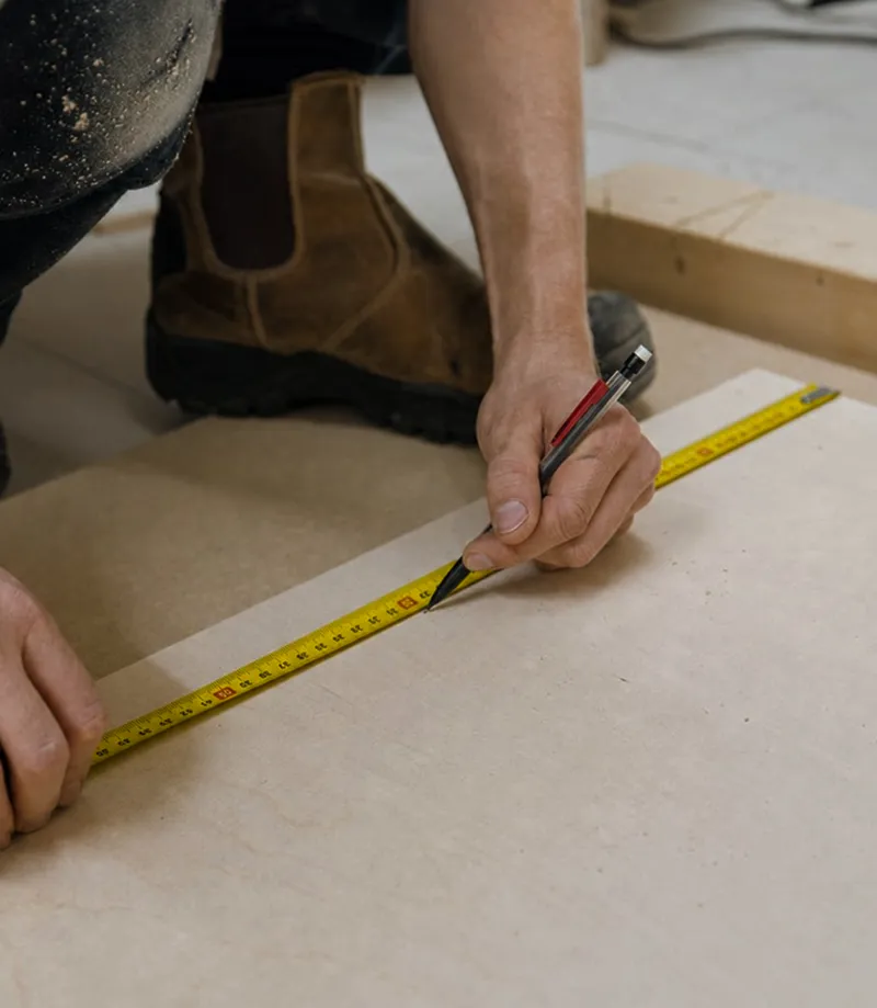 Un artisan prend des mesures sur une plaque de contreplaqué 