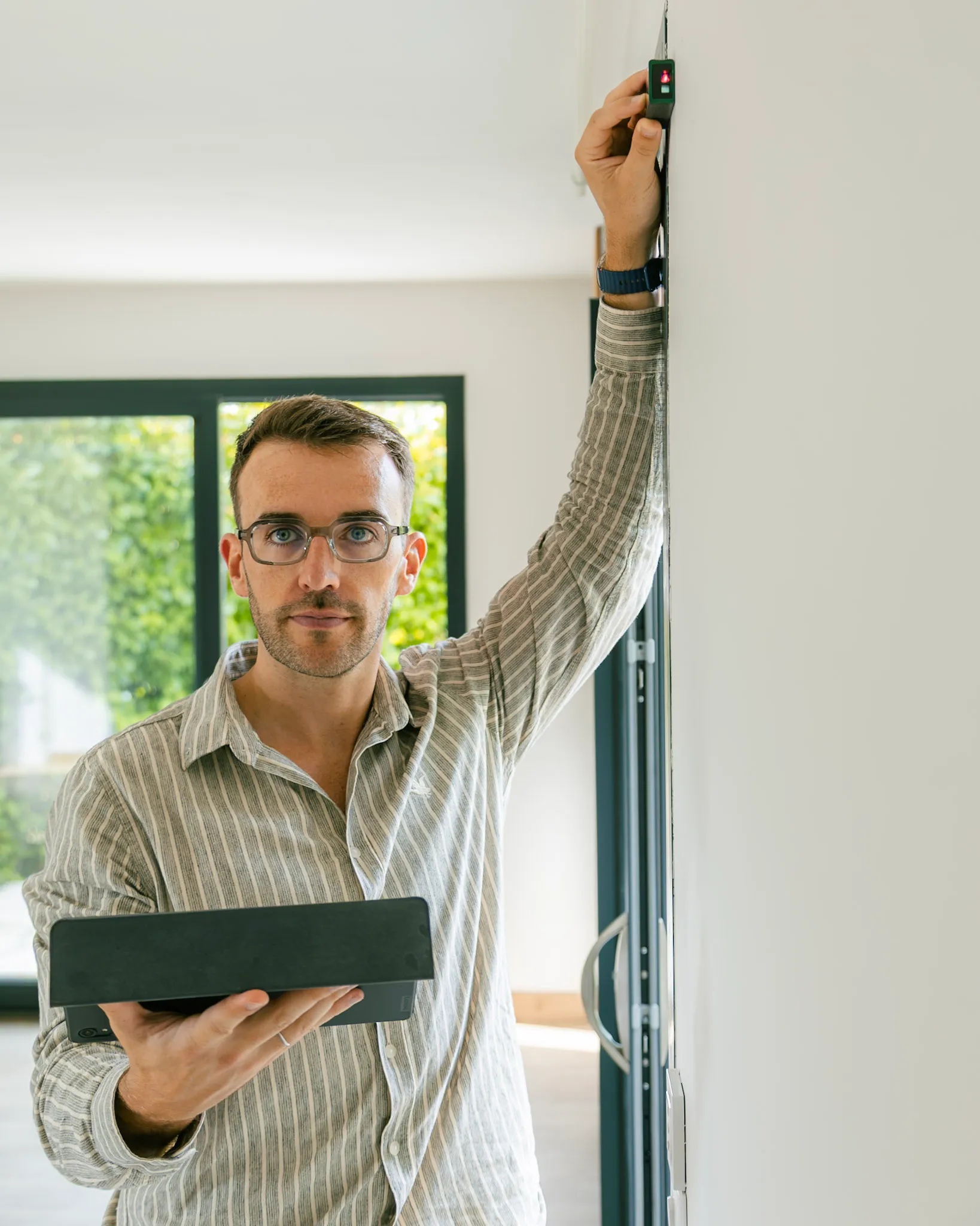 L'agent immobilier Aymeric, prend les mesure d'un mur à l'aide d'un outil électronique