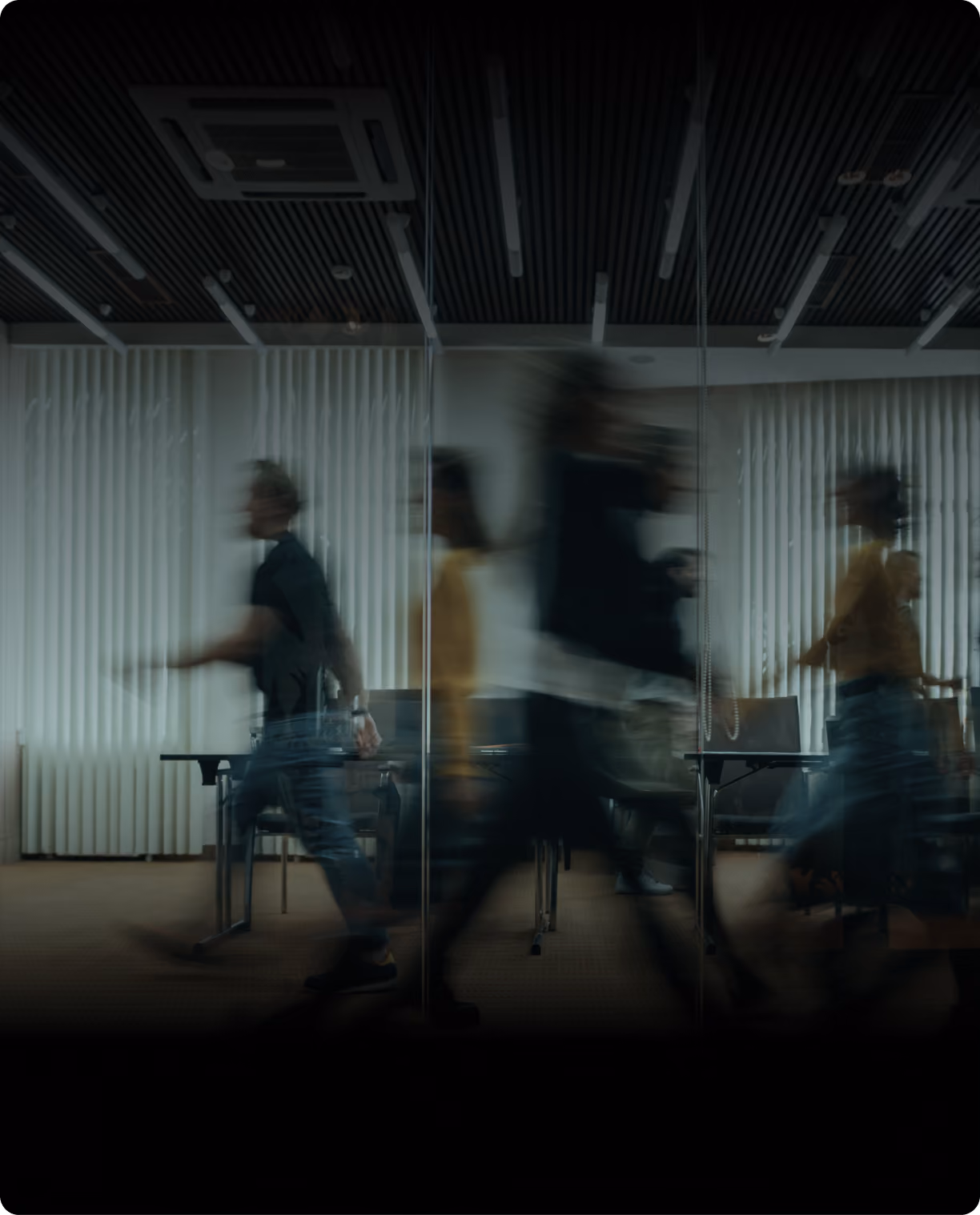 Motion-blurred figures walking past a glass-walled meeting room