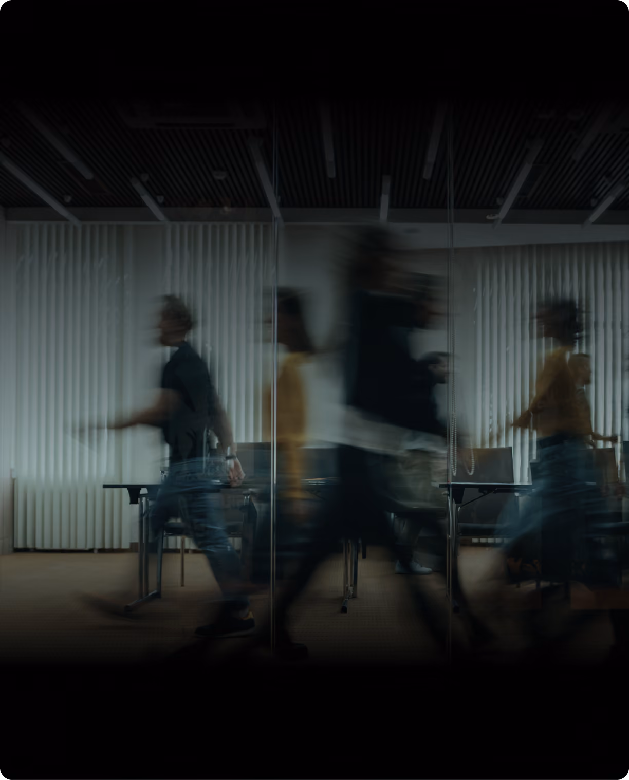 Motion-blurred figures walking past a glass-walled meeting room