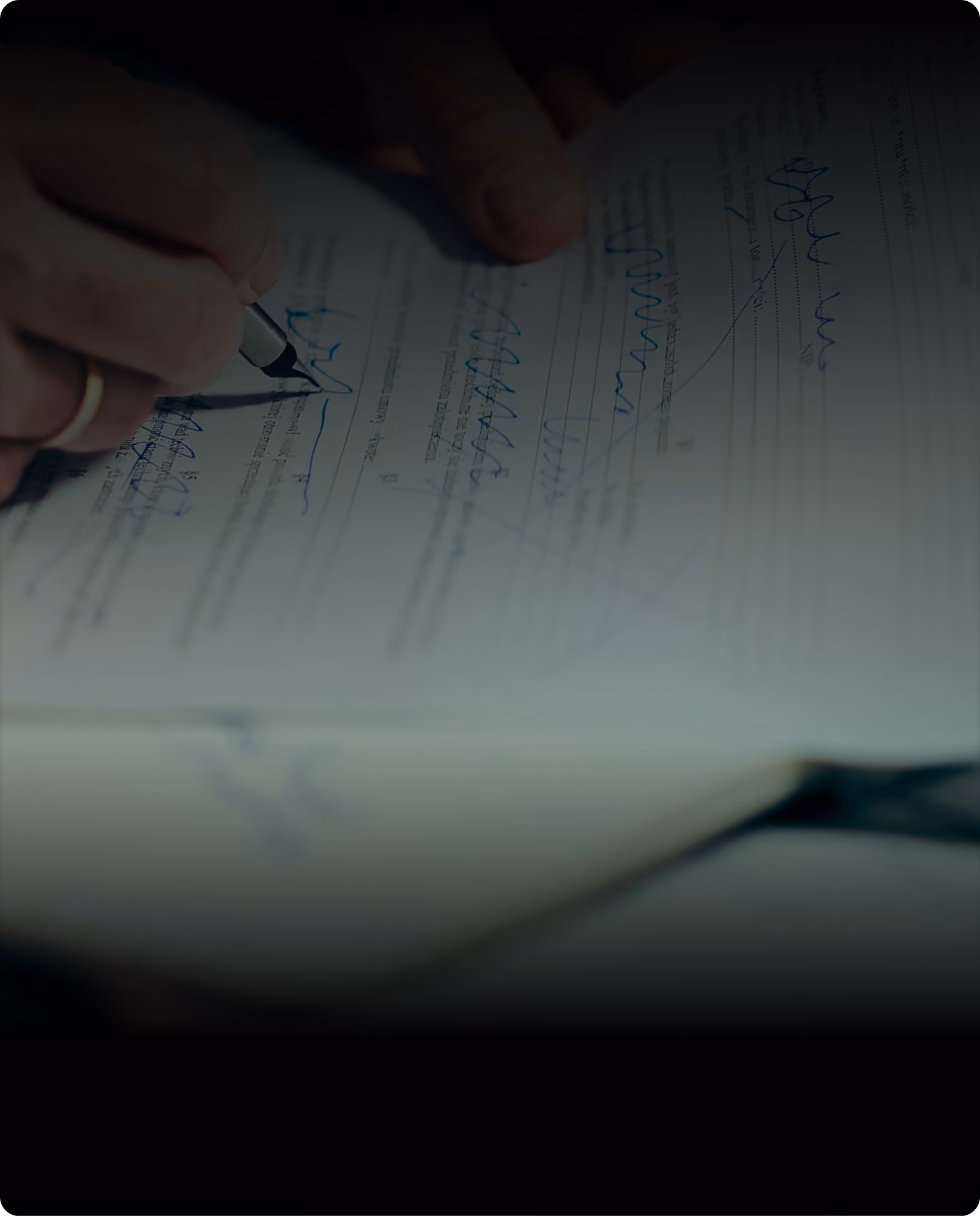 A hand signing a marked-up contract in low light