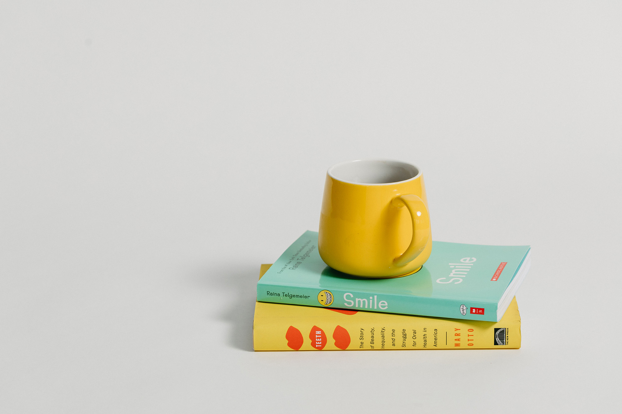 Yellow mug on top of two stacked books titled Smile and Teeth on a white background.