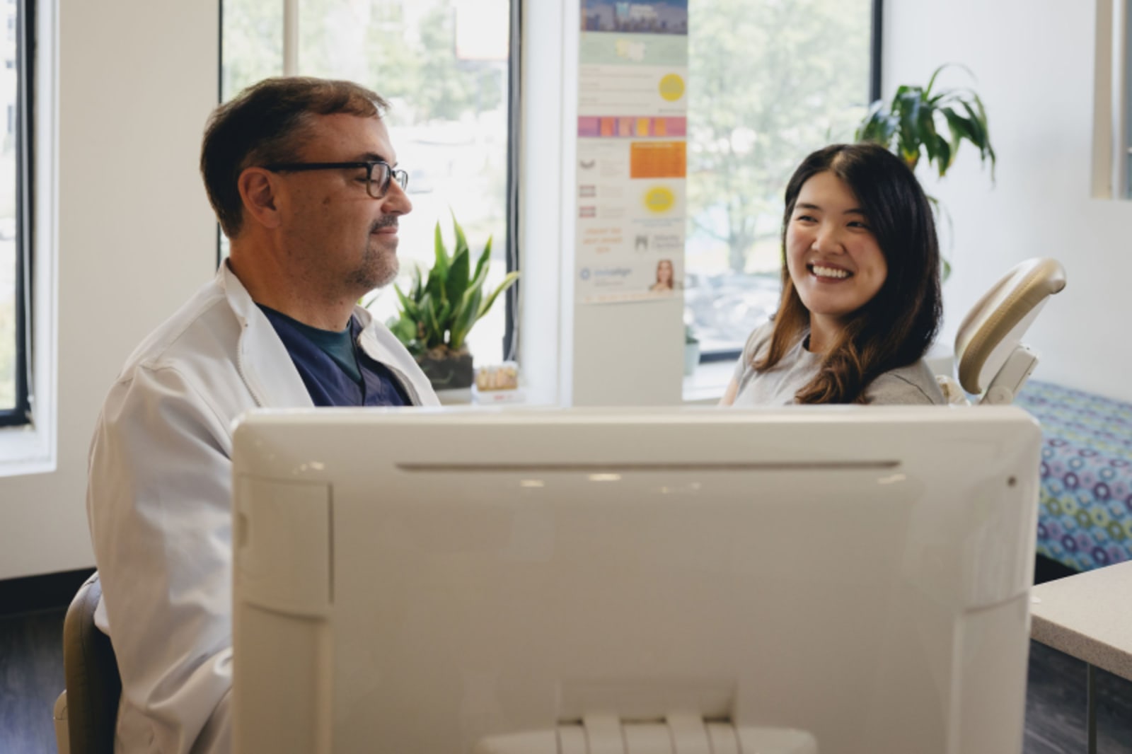 Male dentist consulting with female patient at reception desk in clinical setting