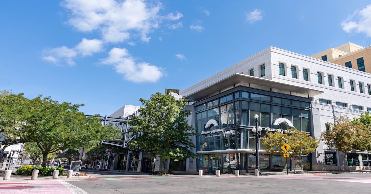Modern glass building labeled 'discovery gateway' on a sunny day with some trees and a few clouds in the blue sky.