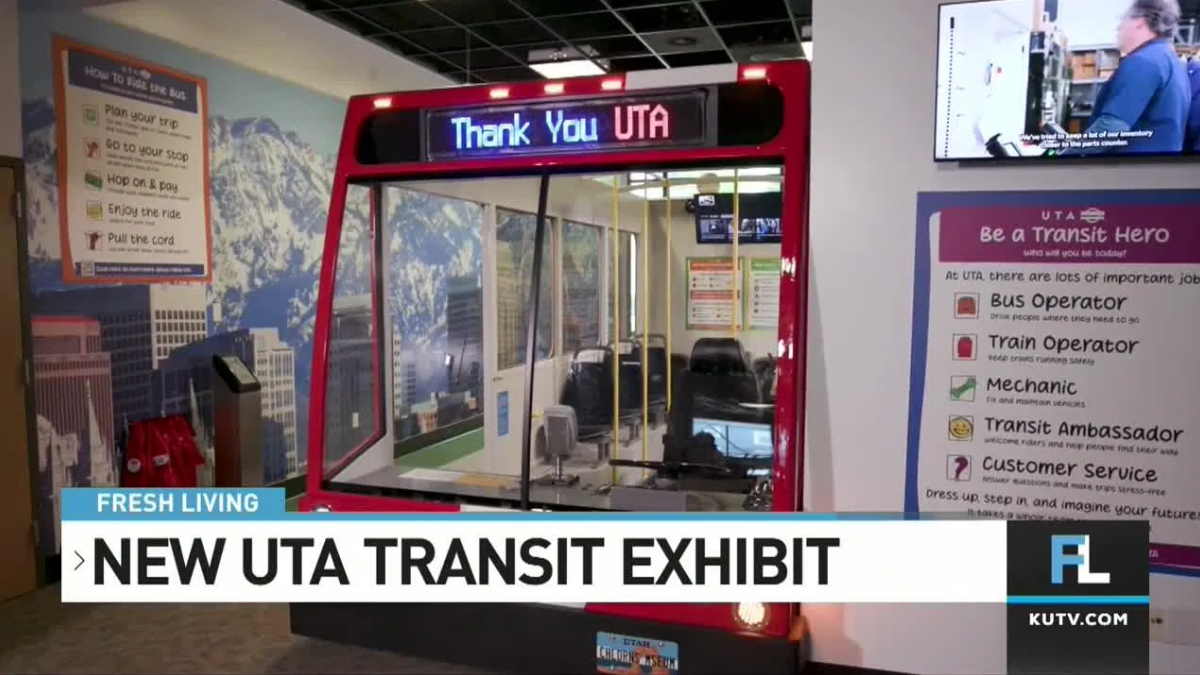 Indoor exhibit featuring the front section of a red UTA transit train with digital sign reading 'Thank You UTA,' surrounded by informational transit posters and a news banner stating 'New UTA Transit Exhibit' from KUTV.