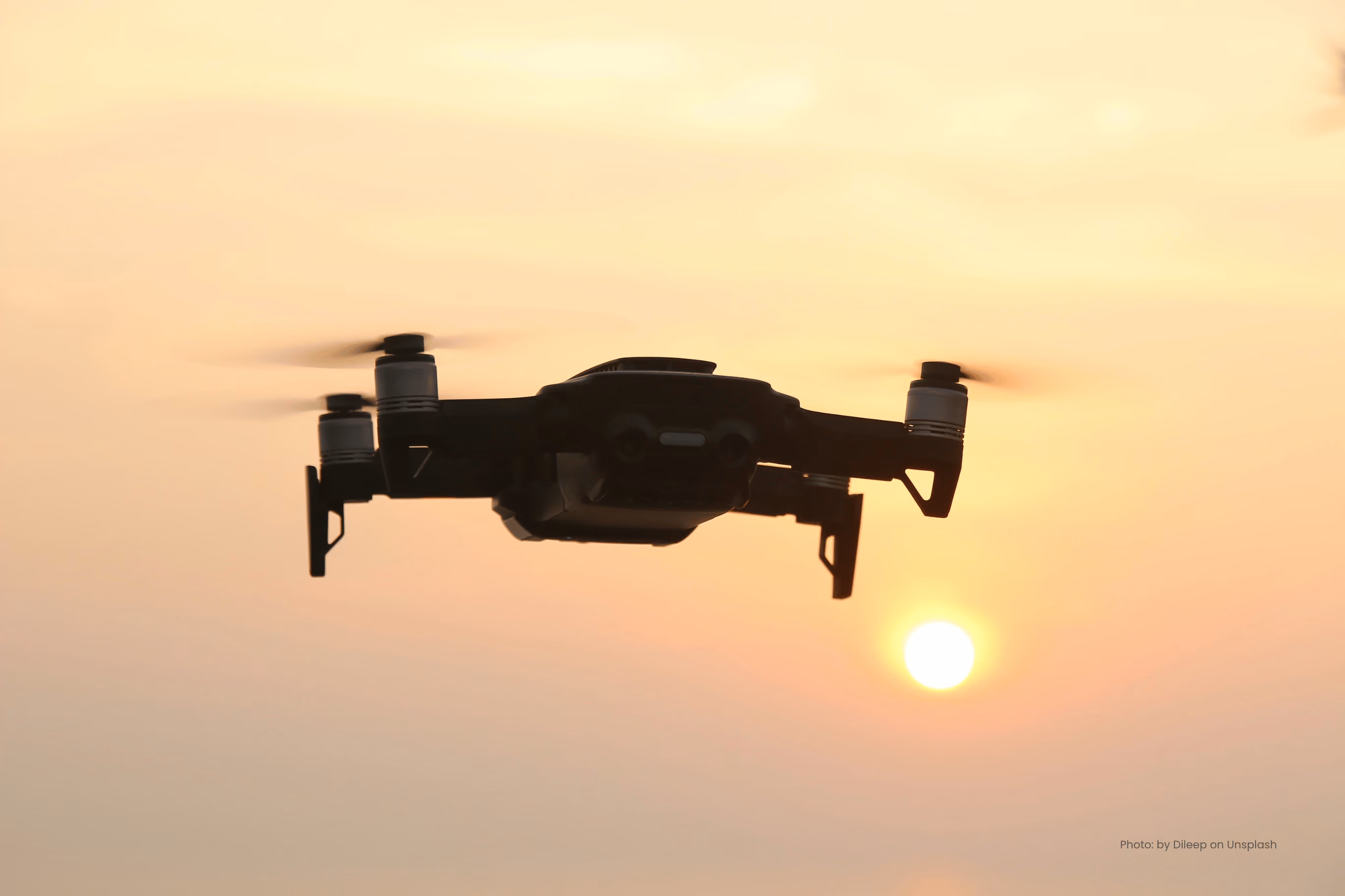 Silhouette of a drone hovering against a sunset sky