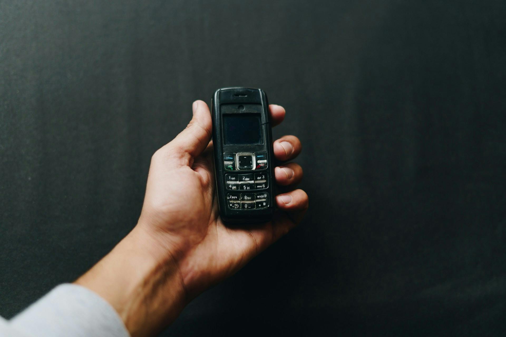 Hand holding a black mobile phone with a physical keypad.