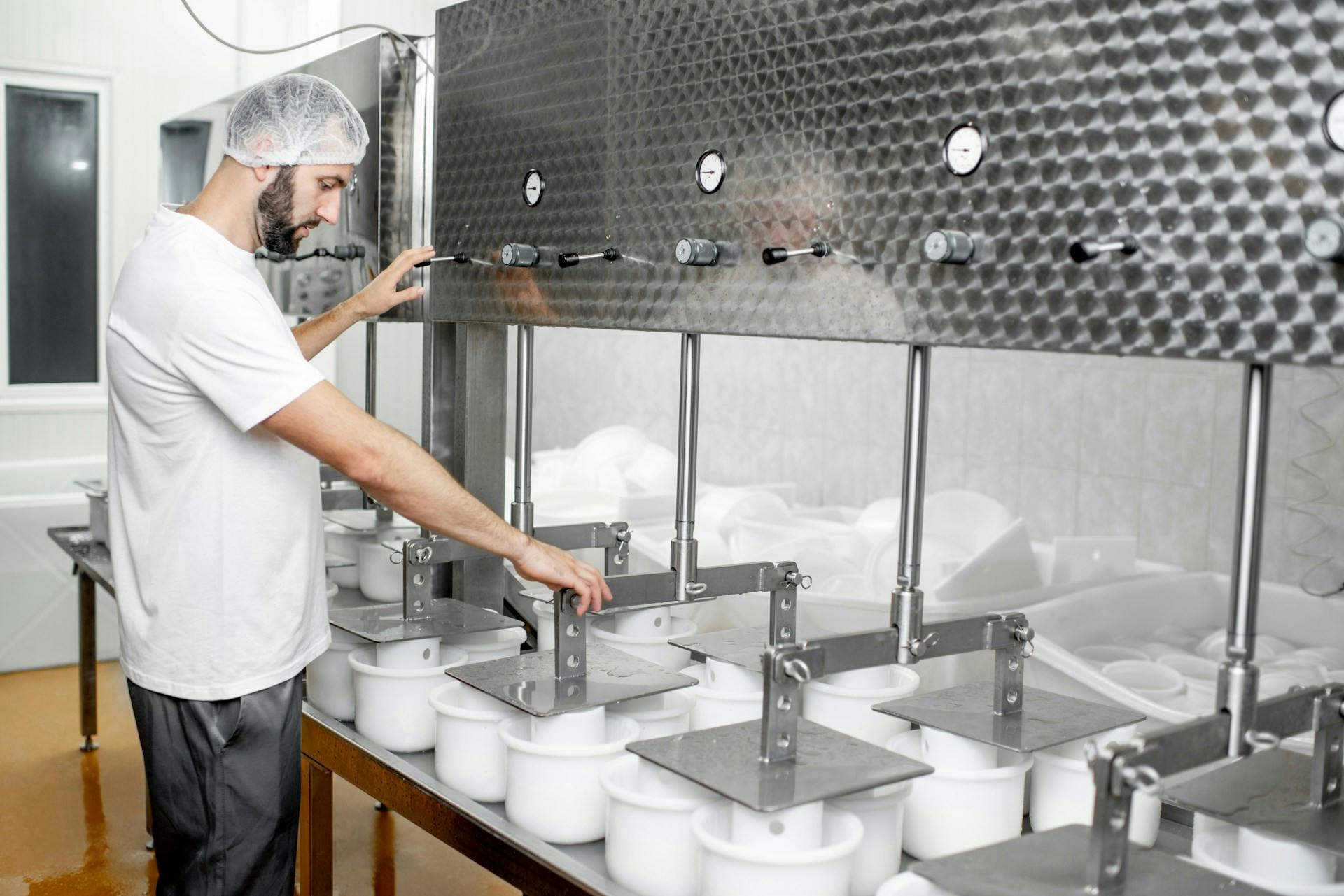 Worker wearing a hairnet operating stainless steel processing equipment.