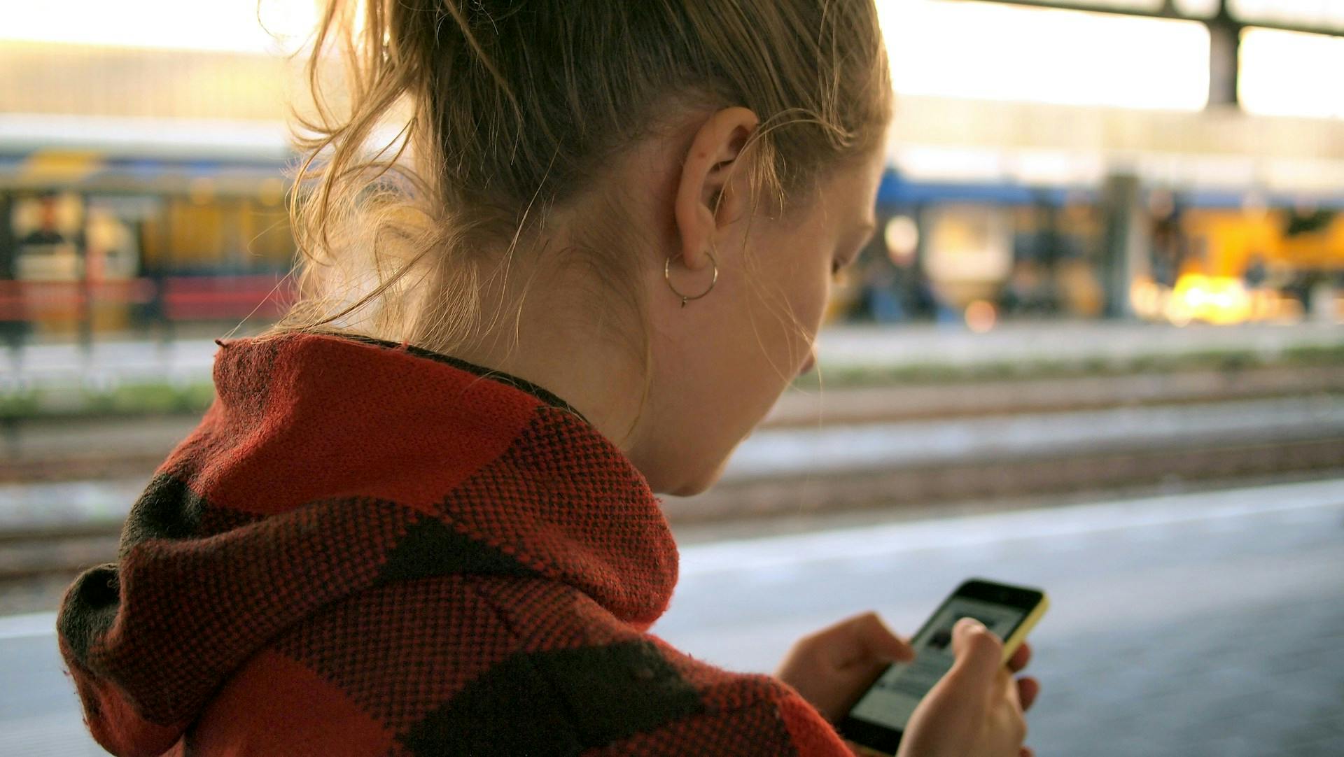 Person checking a mobile phone on a train platform.