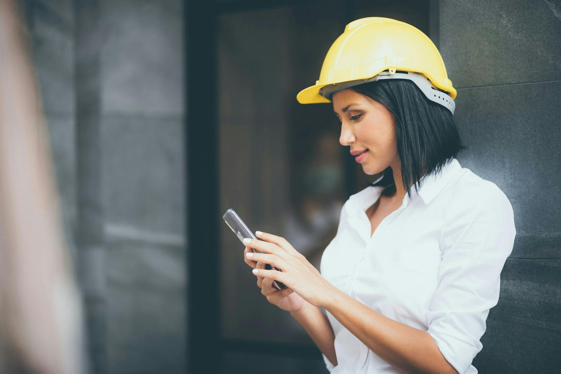 Worker in a yellow hard hat looking at a mobile phone.