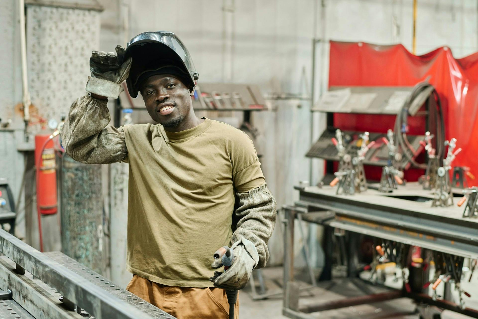 Smiling welder lifting a protective helmet in a workshop.