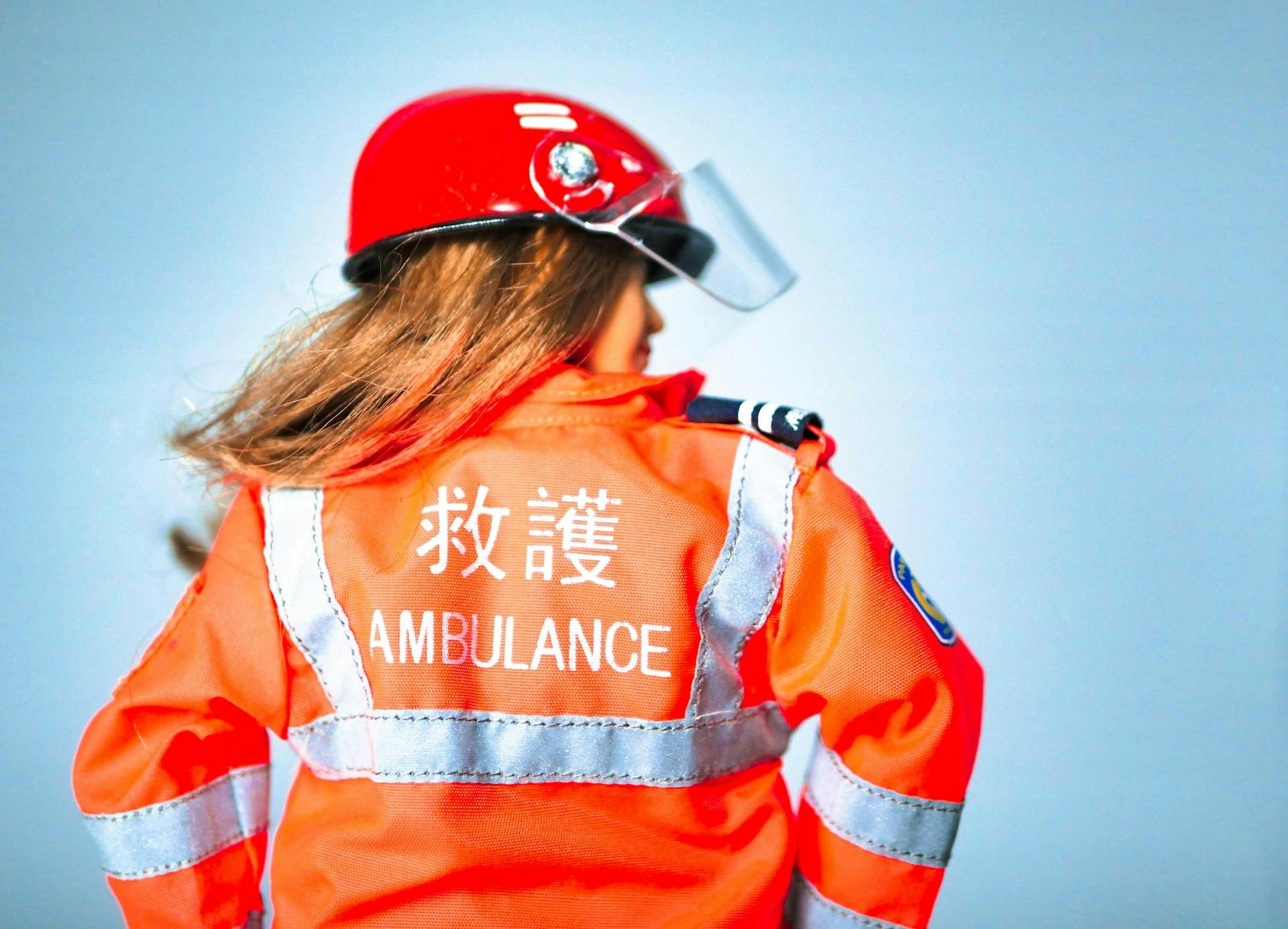 Emergency responder in a red helmet and orange reflective jacket labeled AMBULANCE and Chinese characters.