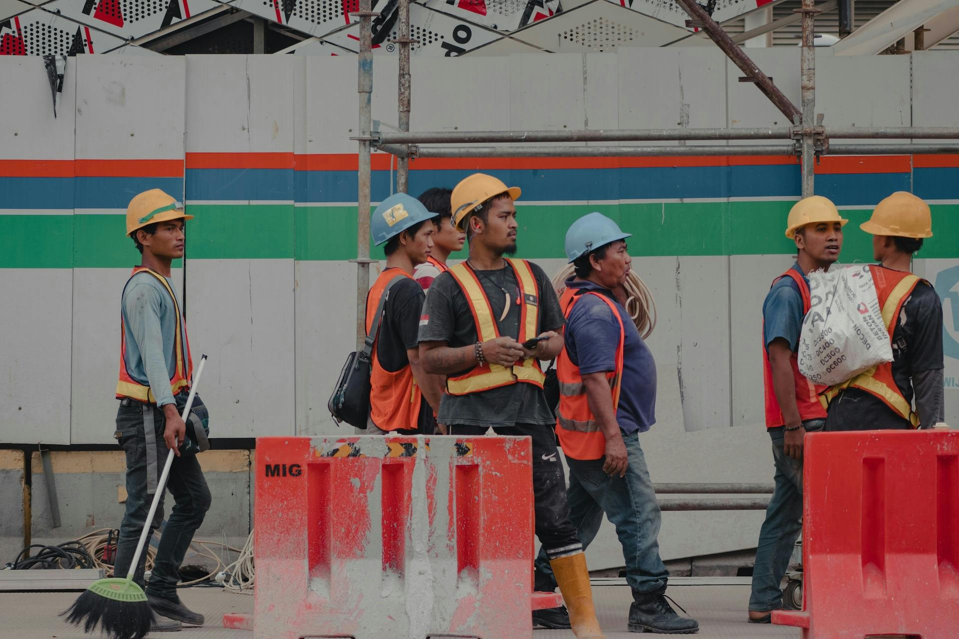 Construction workers in hard hats and reflective vests standing beside scaffolding and red barriers.