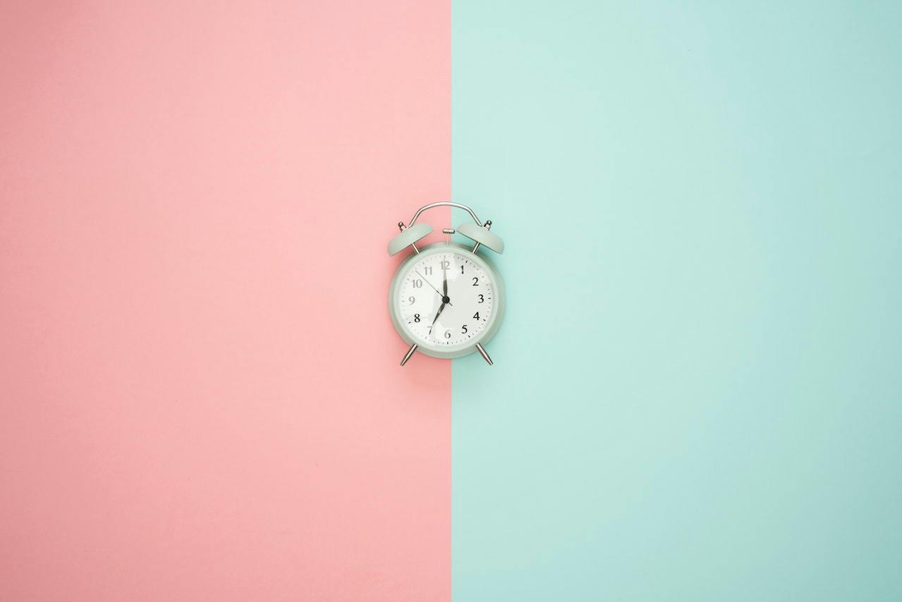 Alarm clock against a background split into pink and mint green halves.