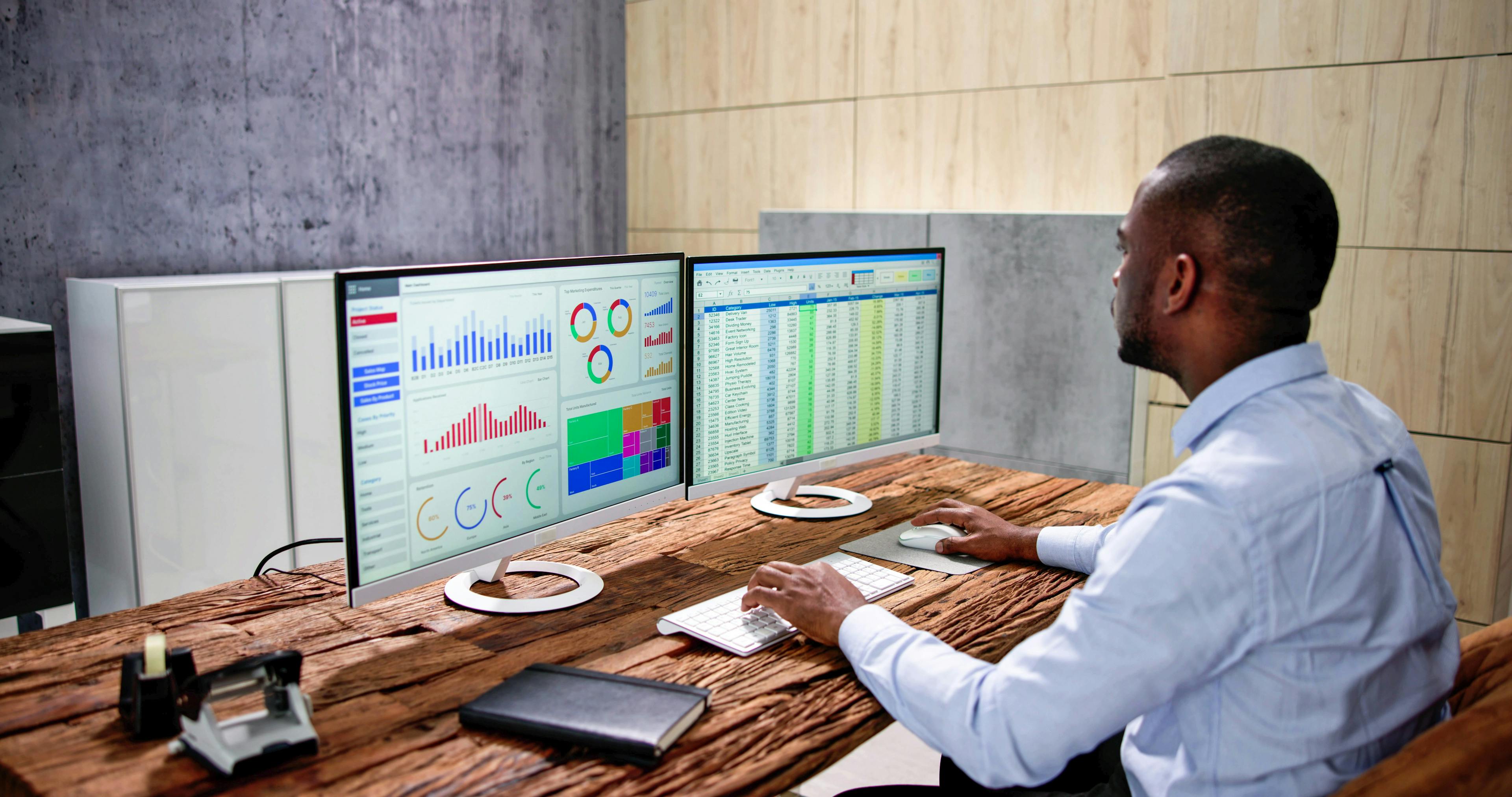 Analyst reviewing workforce dashboard and spreadsheet on dual monitors