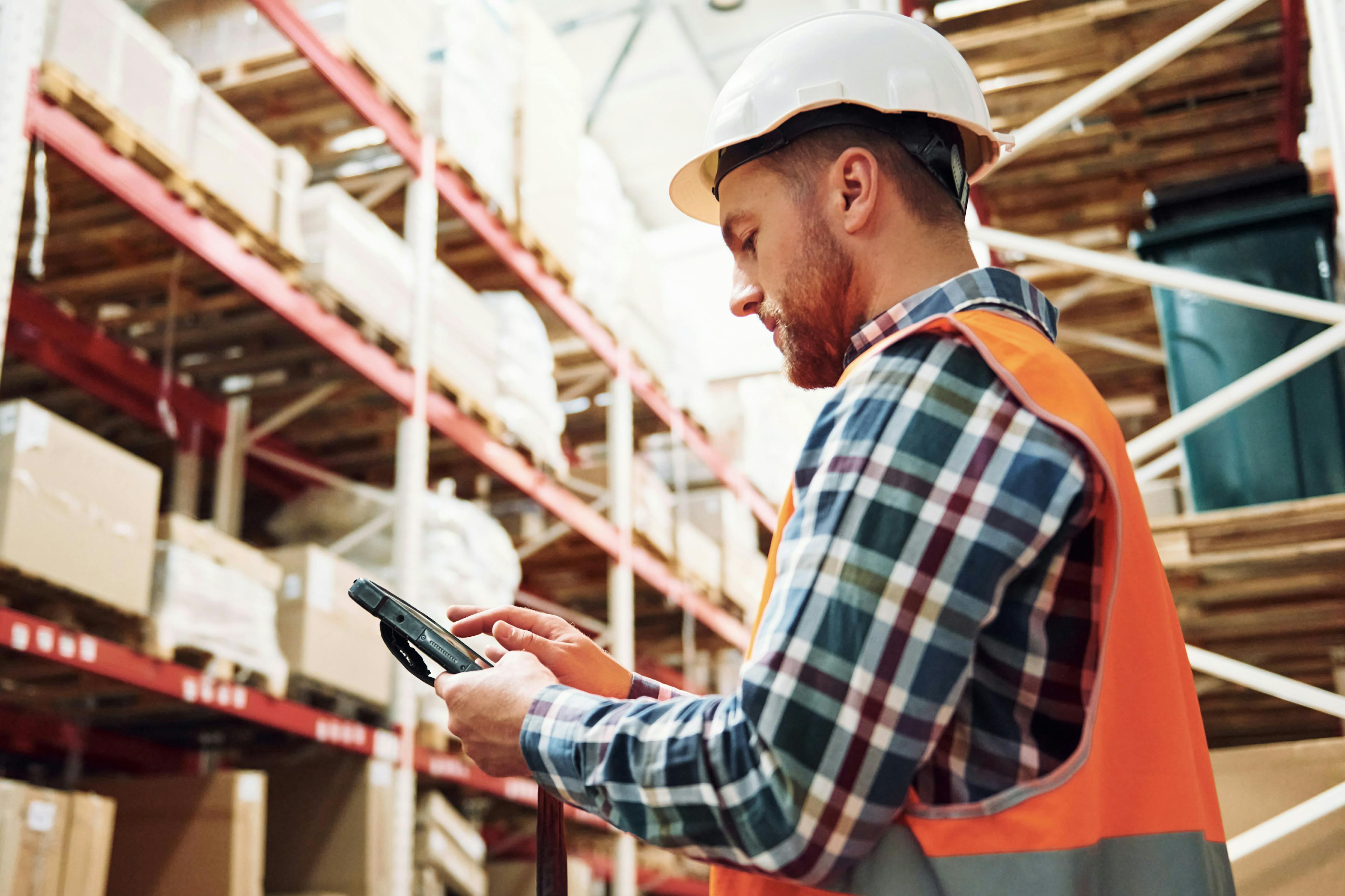 Warehouse worker in hard hat checking phone 